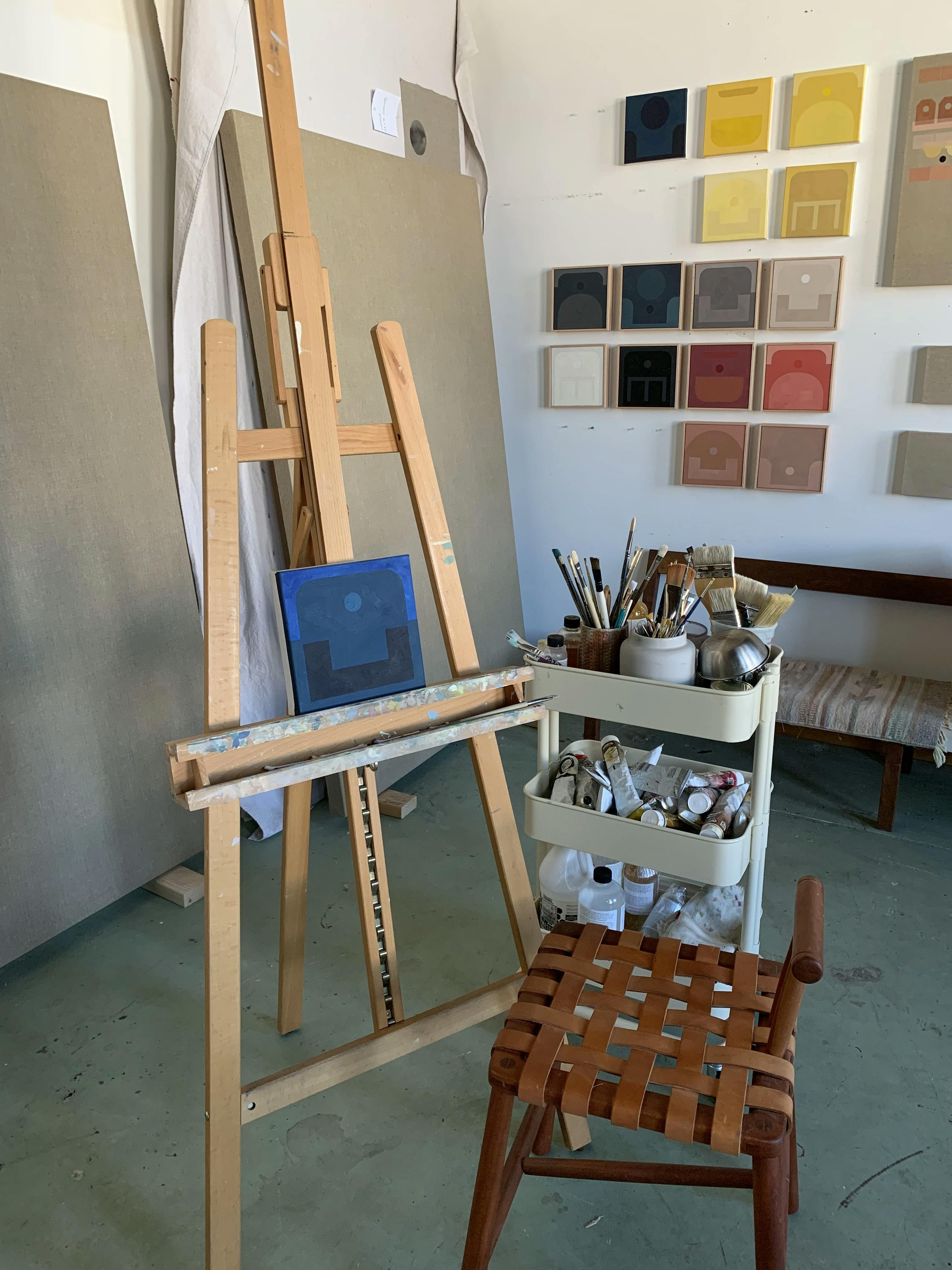 An easel with a small blue painting by artist Carla Weeks inside of her studio.