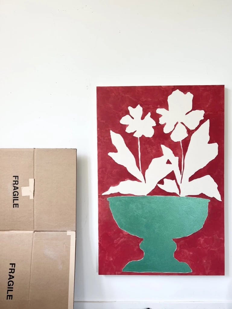 A red painting with a bouquet of flowers in a green vase by artist Kate Roebuck pinned to a white wall in her studio.