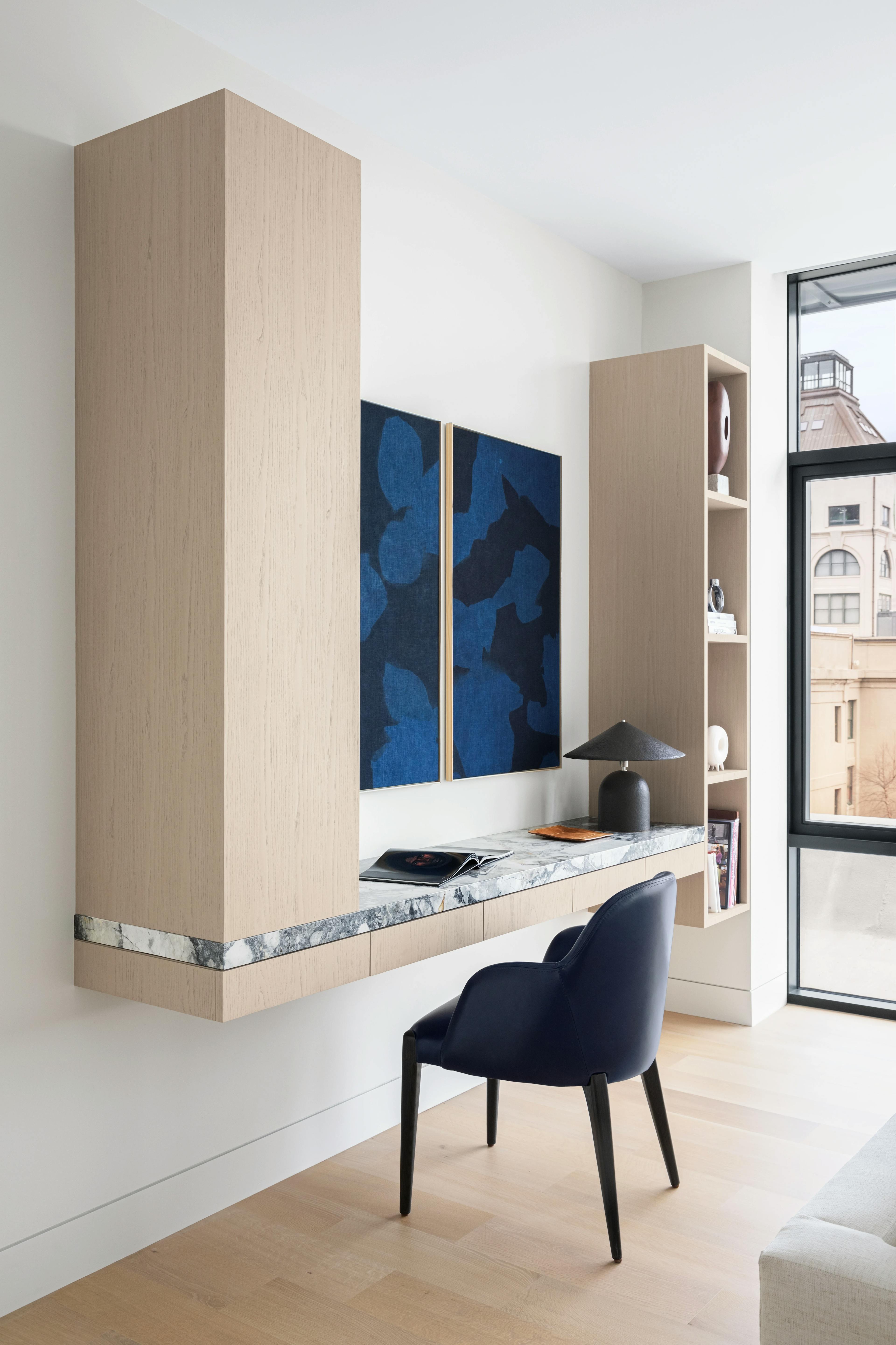 Blue and black diptych by artist Carrie Crawford installed over a beige floating desk in a modern living room.