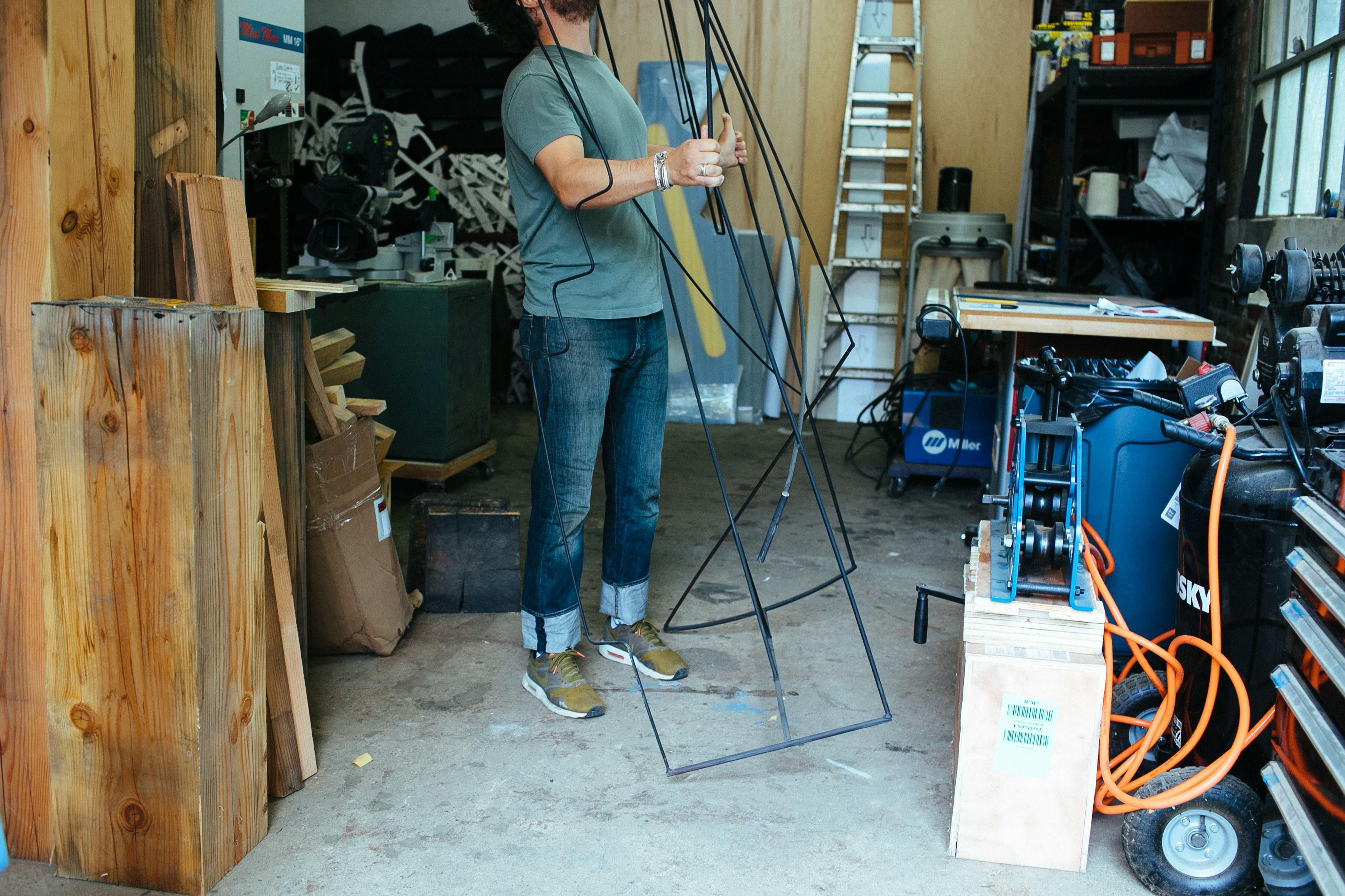 Artist Fitzhugh Karol holding a tall wire sculpture in his studio.