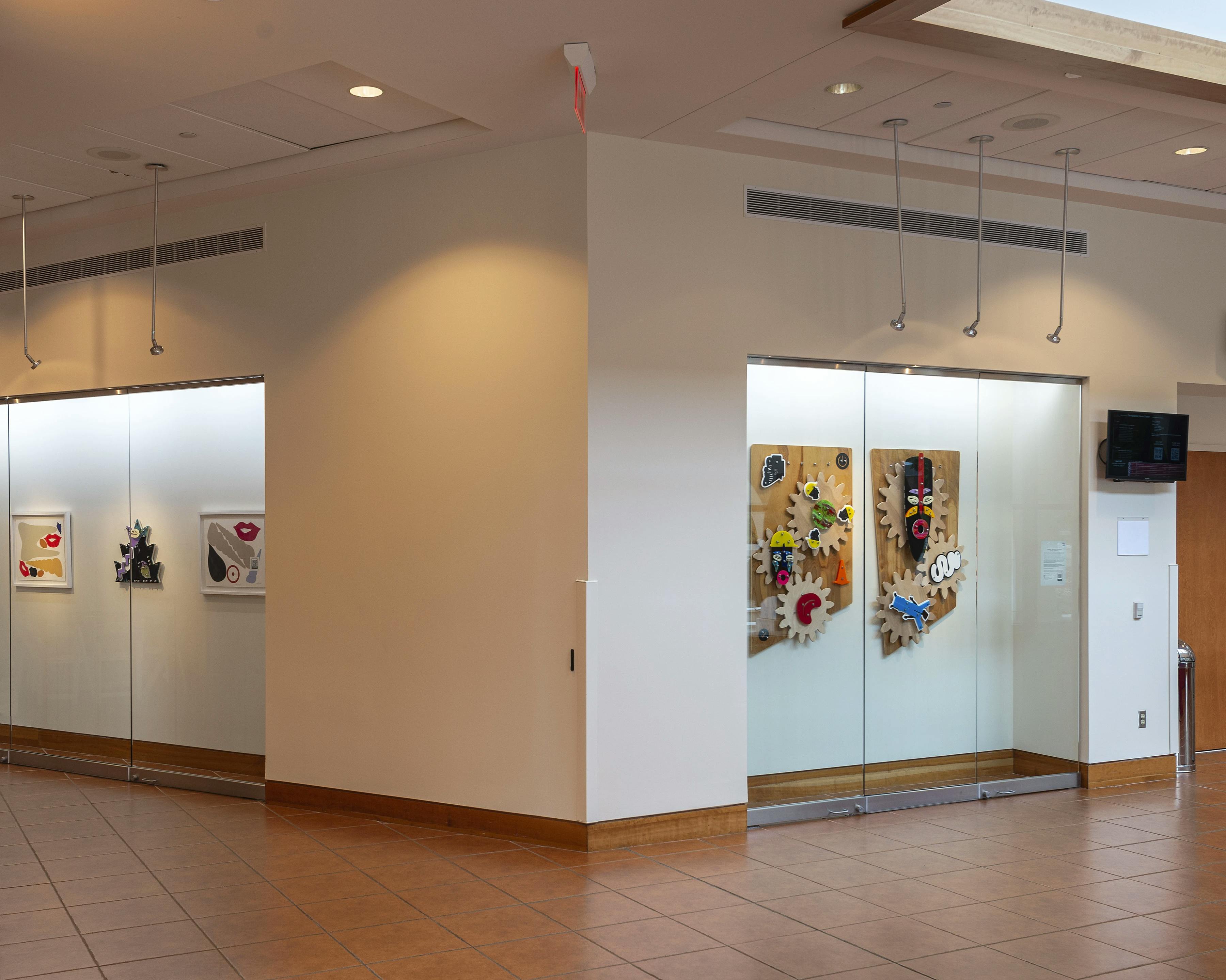 Two framed digital prints and three abstract wall sculptures by artist Damien Davis installed on a white wall behind a glass case at Montclair State University.