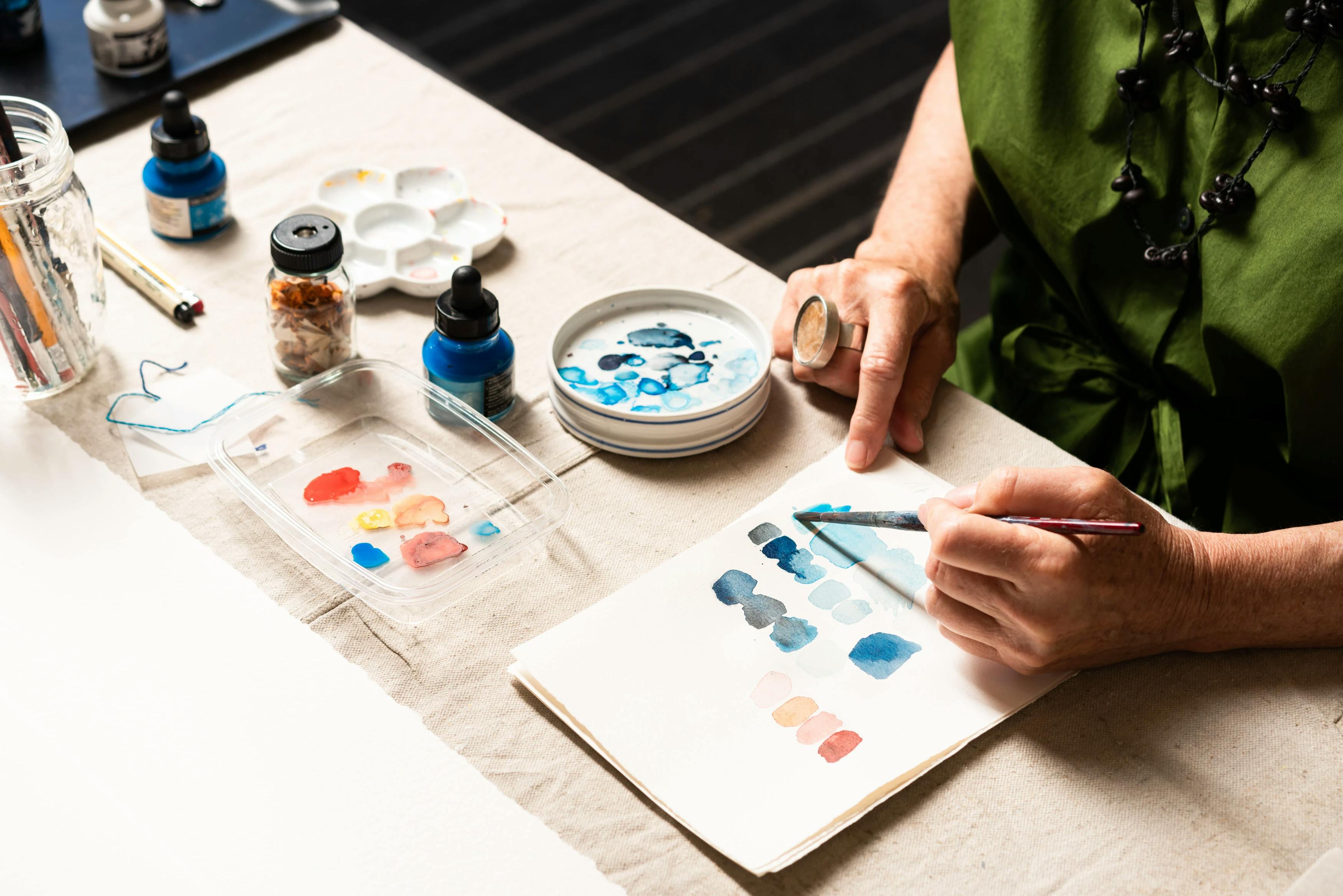 Artist Gail Tarantino using a small paintbrush to mix acrylic paints on paper.