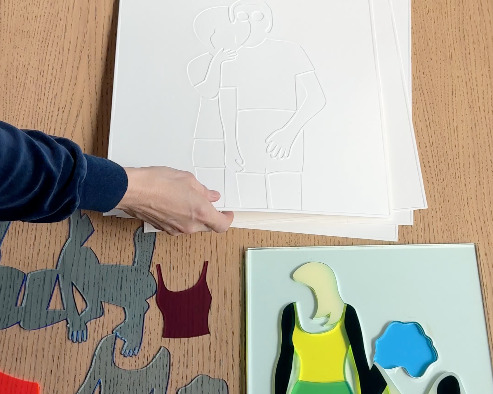 Artist Dana Bell placing a white print on a table next to acrylic cut-outs.
