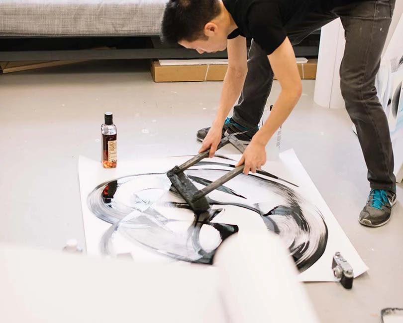 Artist Thomas Hammer using a foam brush to create circulate swaths of black and white ink on paper.
