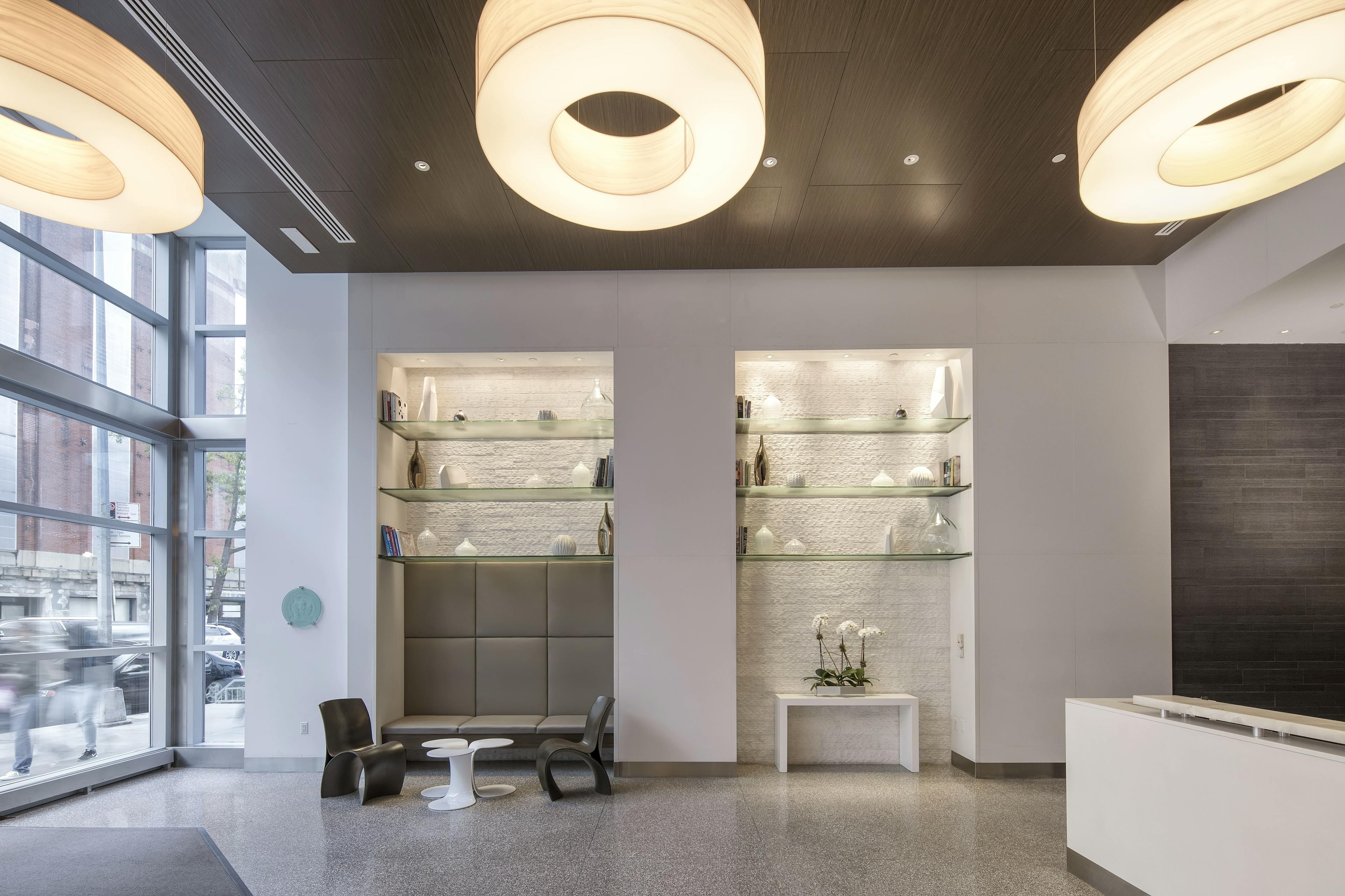 Modern lounge area at DKLB BKLN with three circular lighting fixtures, gray floors, and exposed glass shelves with an assortment of white vessels.