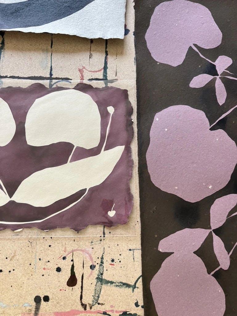 Two purple paintings with cherries by artist Kate Roebuck next to each other on a table in her studio.
