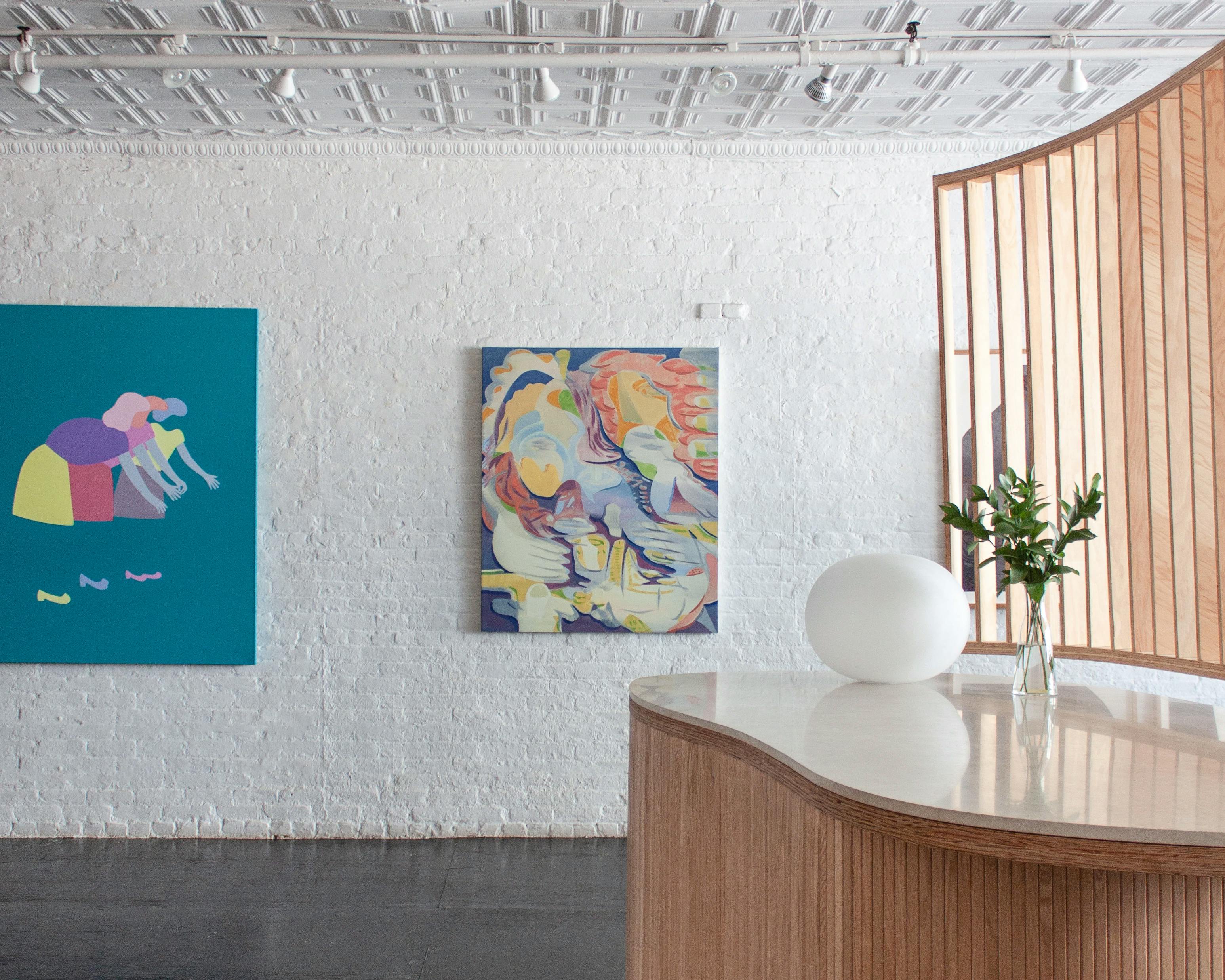 A teal painting of characters reaching by Dana Bell next to a multicolored abstract figure by Trina Turturici installed on a white wall at Uprise Art for the Figurative collection.