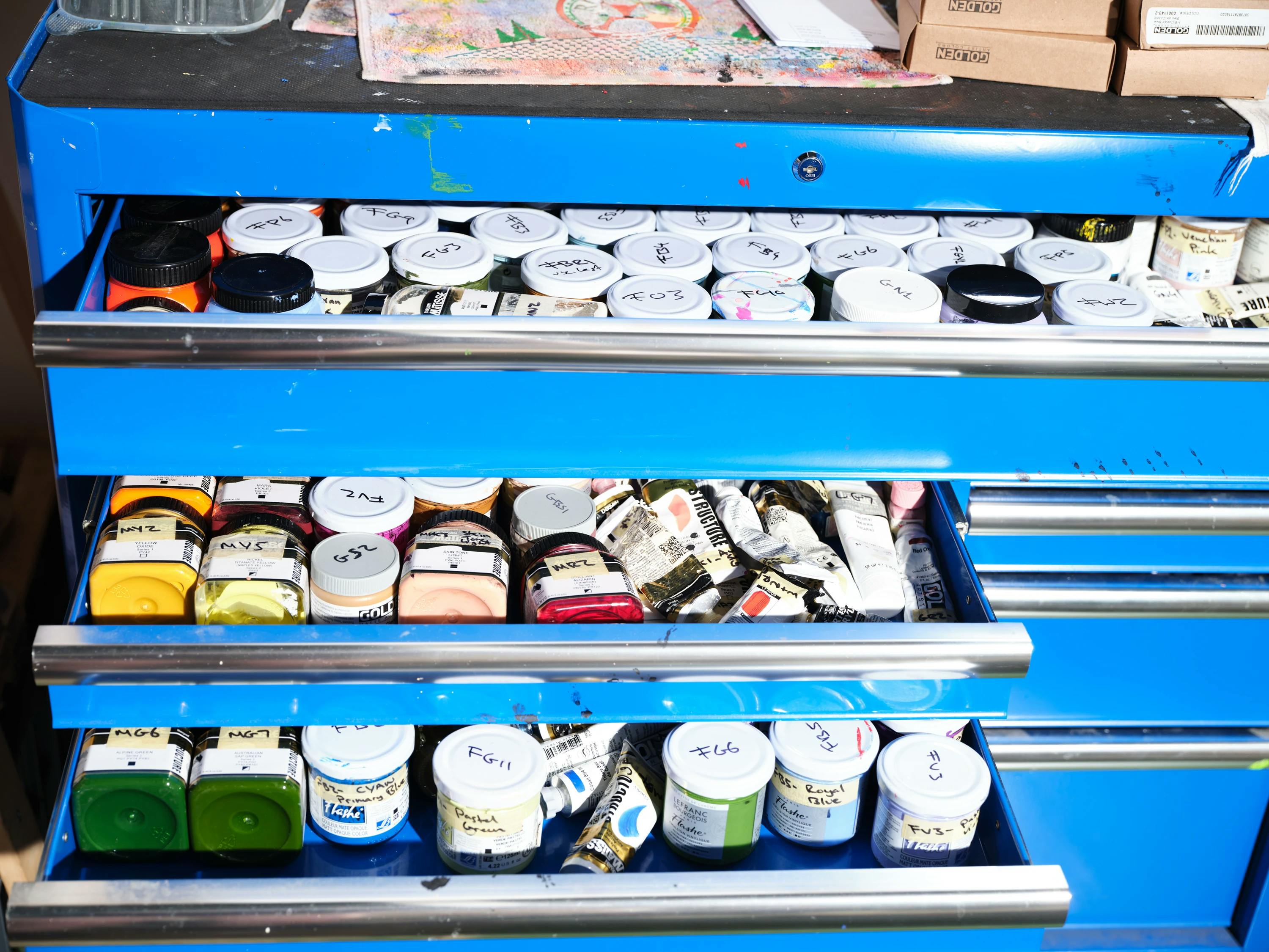 Jars of paint inside blue drawers inside Artist Evi O's studio.