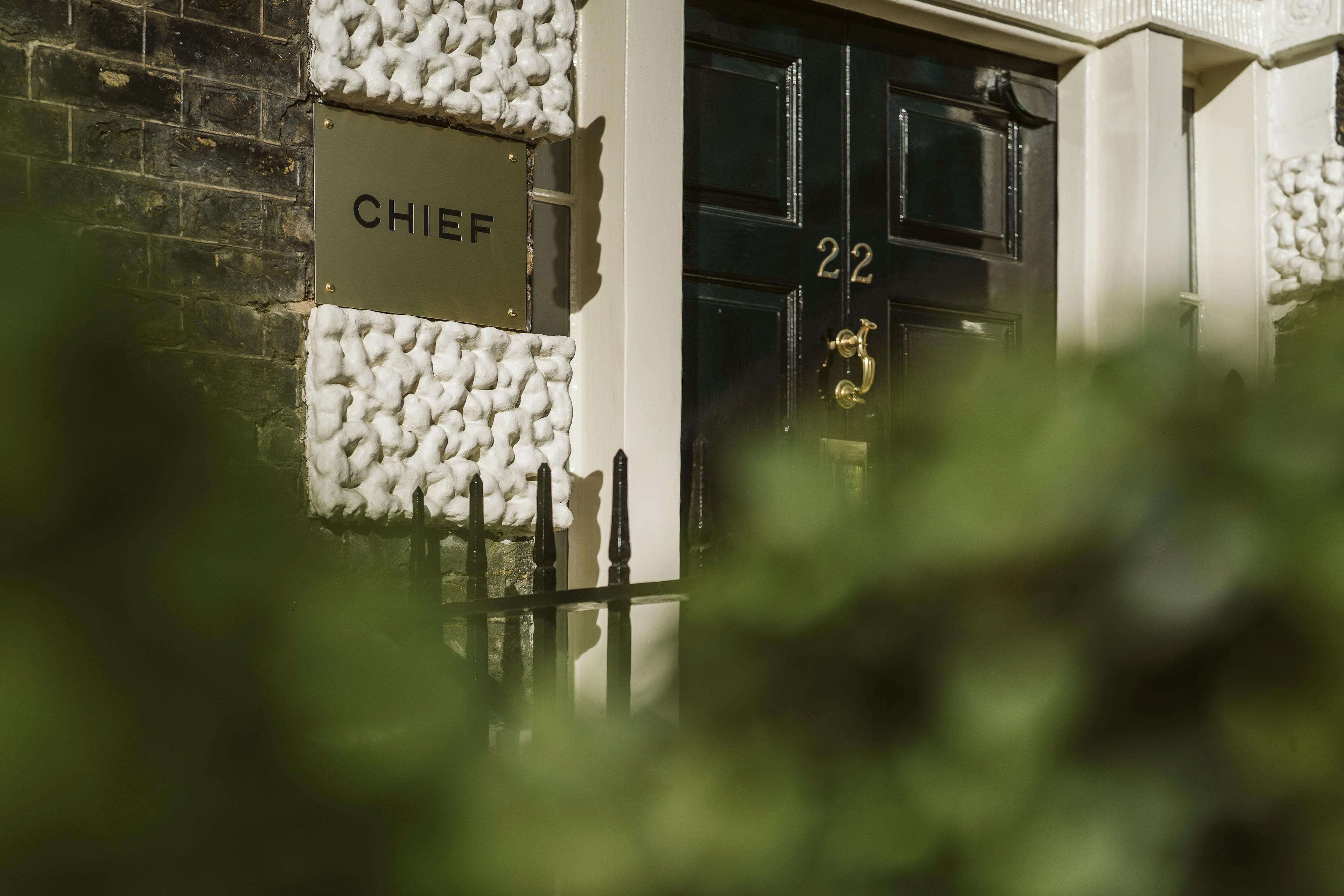 The outdoor entrance to the Chief London clubhouse, featuring a gold sign inscribed with "CHIEF" and a black door with a gold "22".
