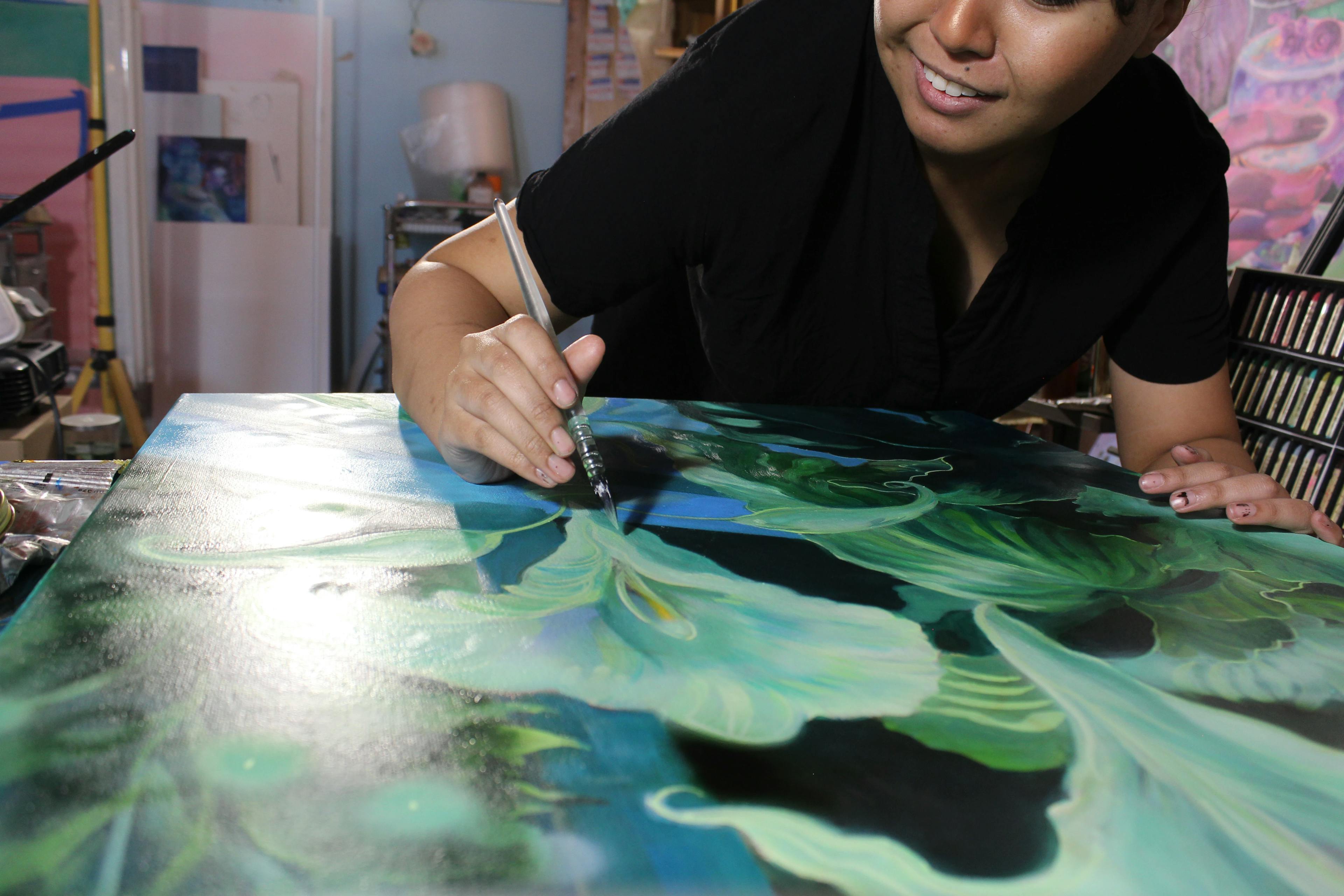Artist Nefertiti Jenkins working on a painting of green and white flowers in her studio.