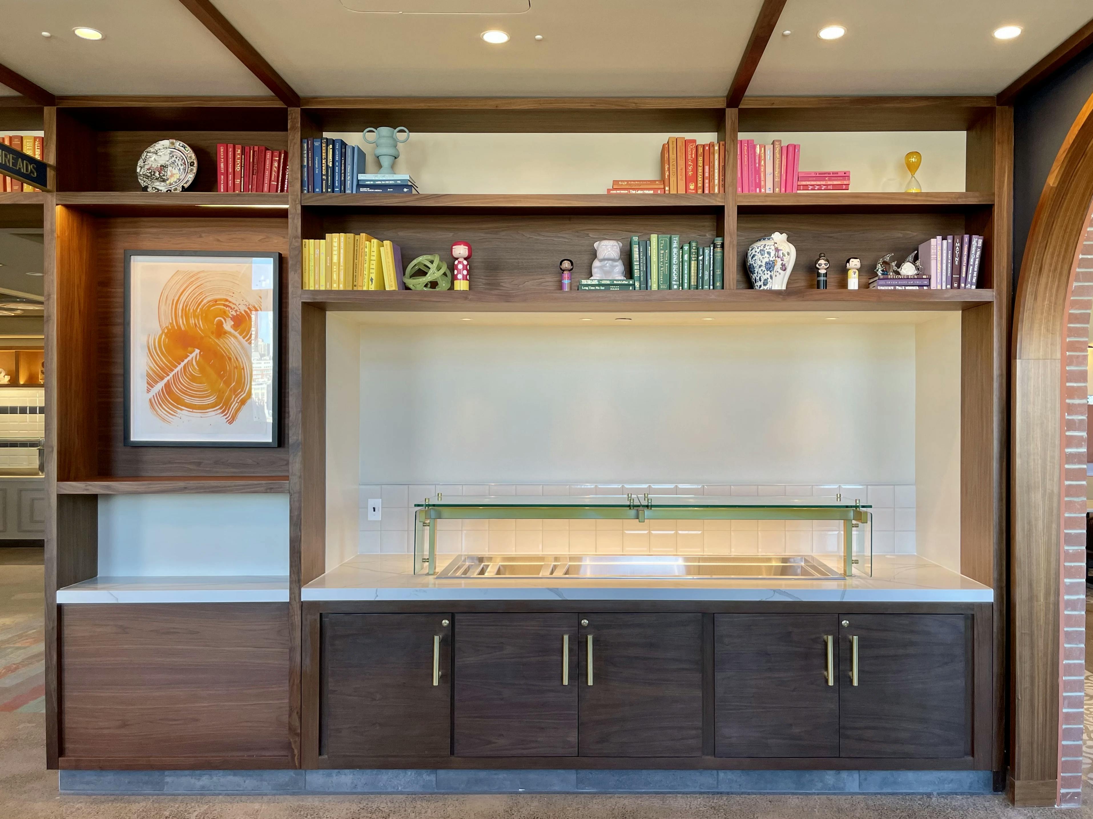 A painting by artist Linda Colletta installed within wooden shelving next to a buffet serving area.