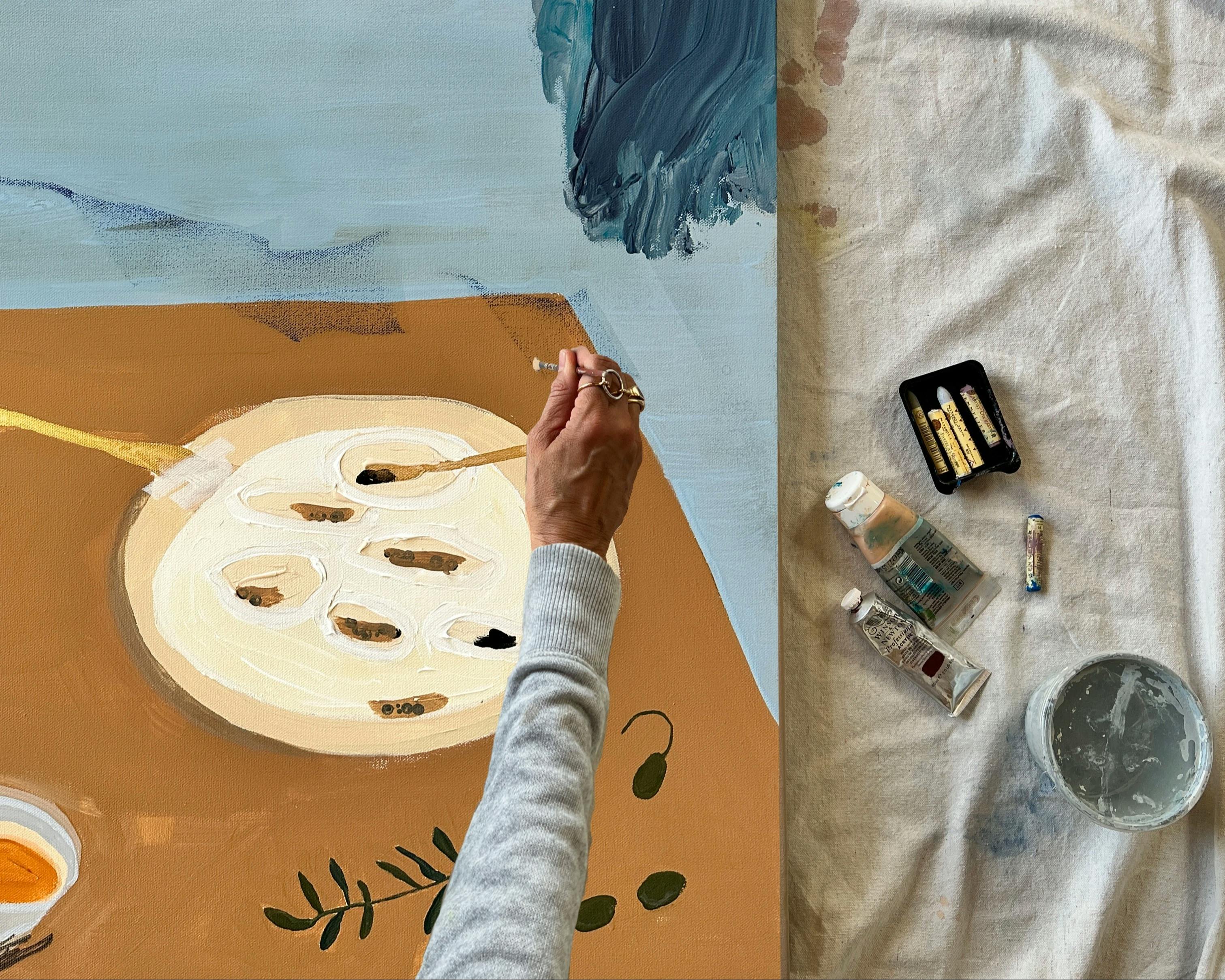 Artist Karina Bania working on a blue, brown and white painting in her studio. 