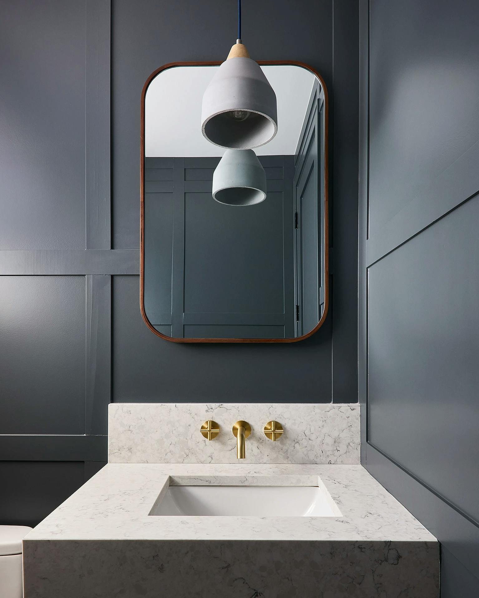 Navy blue bathroom with modern gold faucets and a rectangular iron mirror in a Chicago apartment.