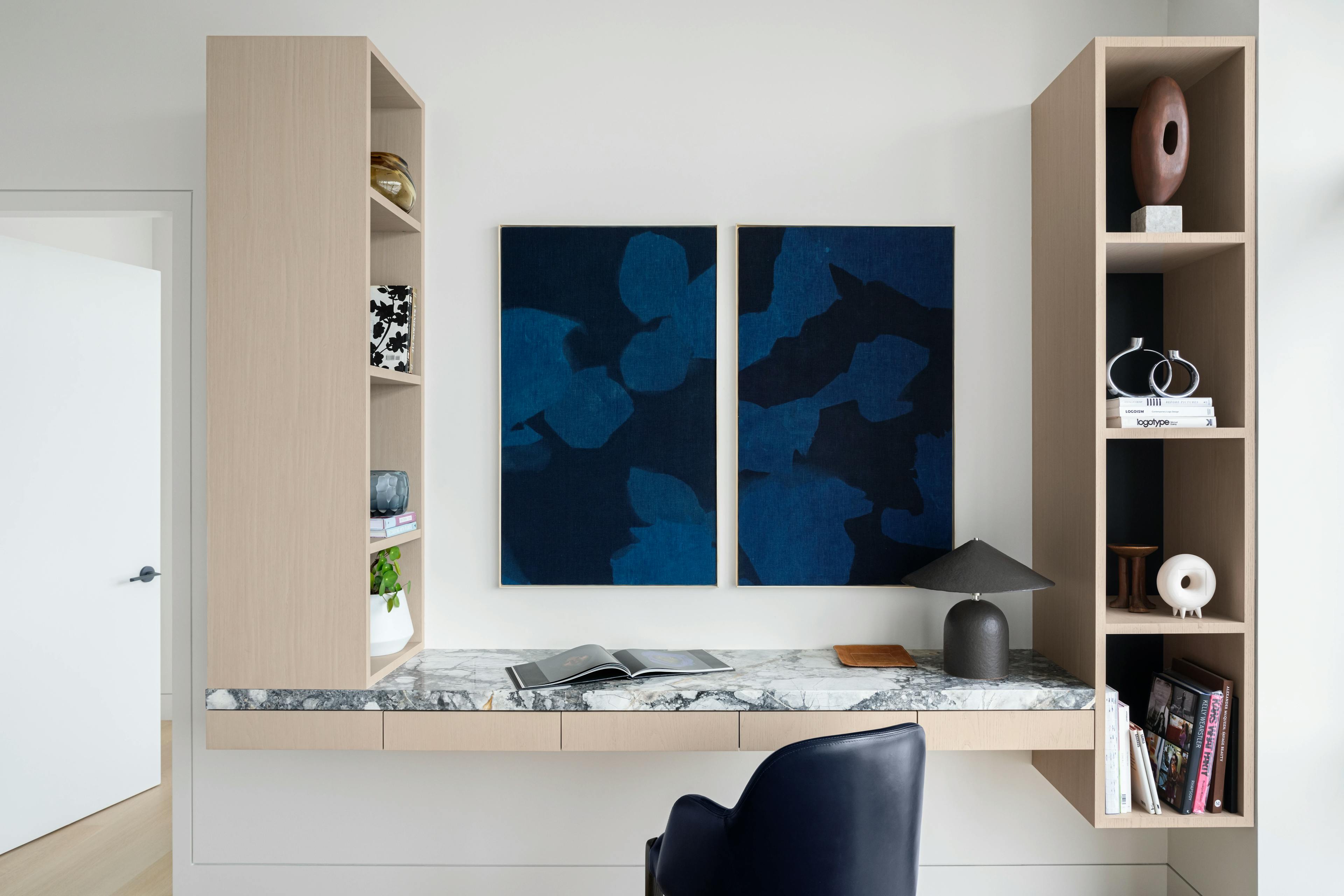 Abstract, blue and black diptych made from organic pigments by artist Carrie Crawford installed above a beige floating desk.