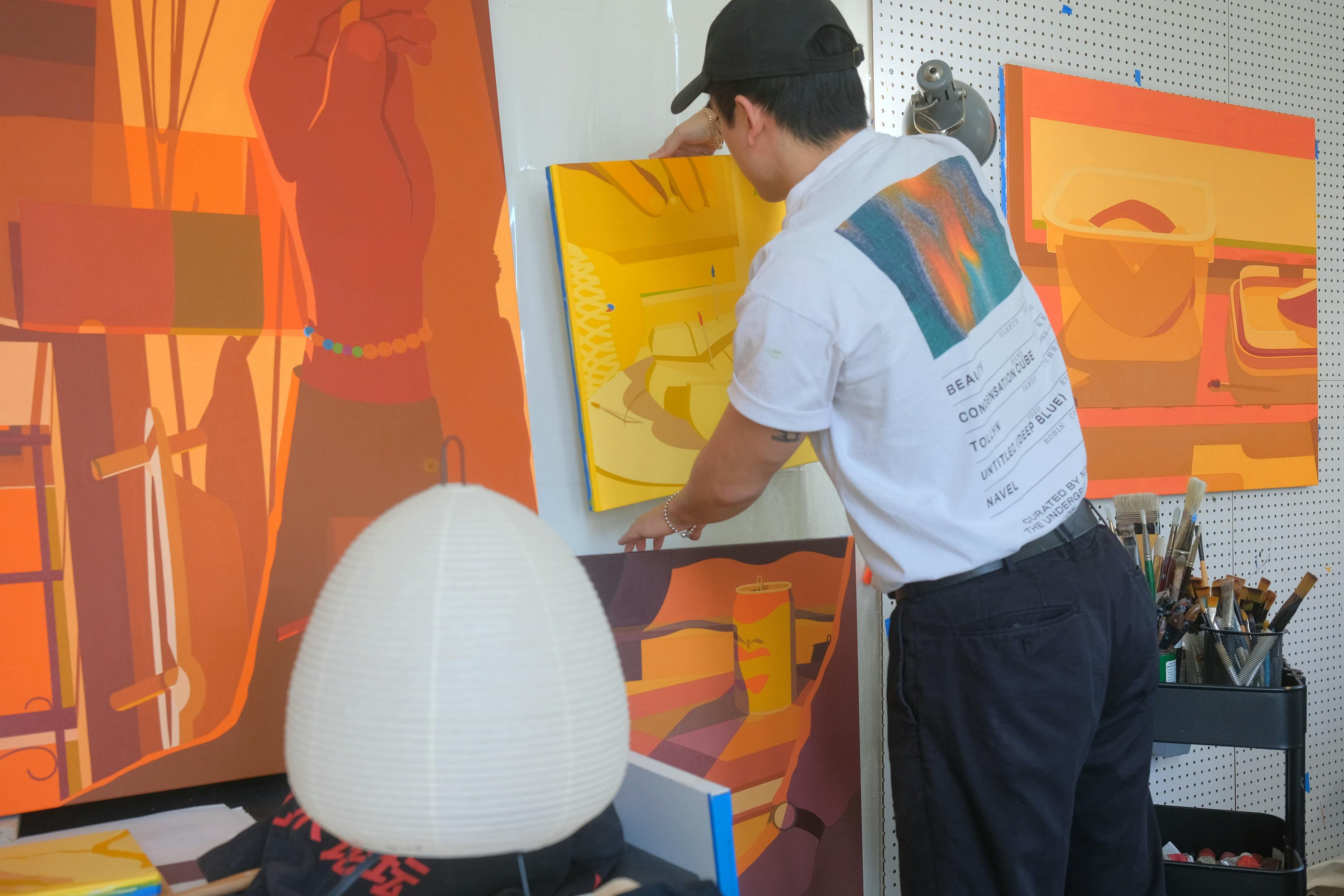 Artist Adrian Kay Wong lifting a yellow painting in his studio. 
