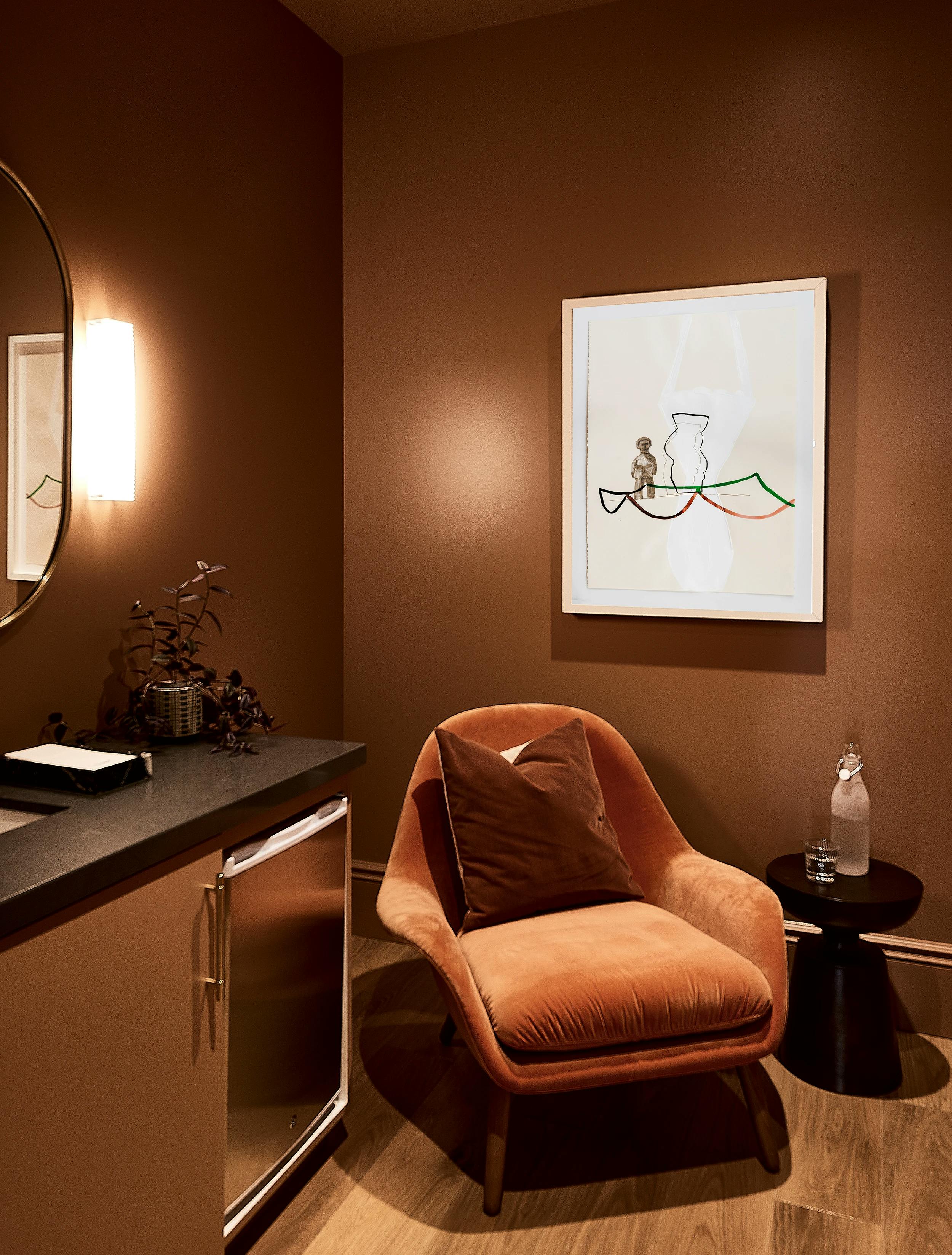 A framed abstract artwork with a figure by artist Vicki Sher on a dark brown wall above a velvet orange chair in the Chief San Francisco clubhouse.