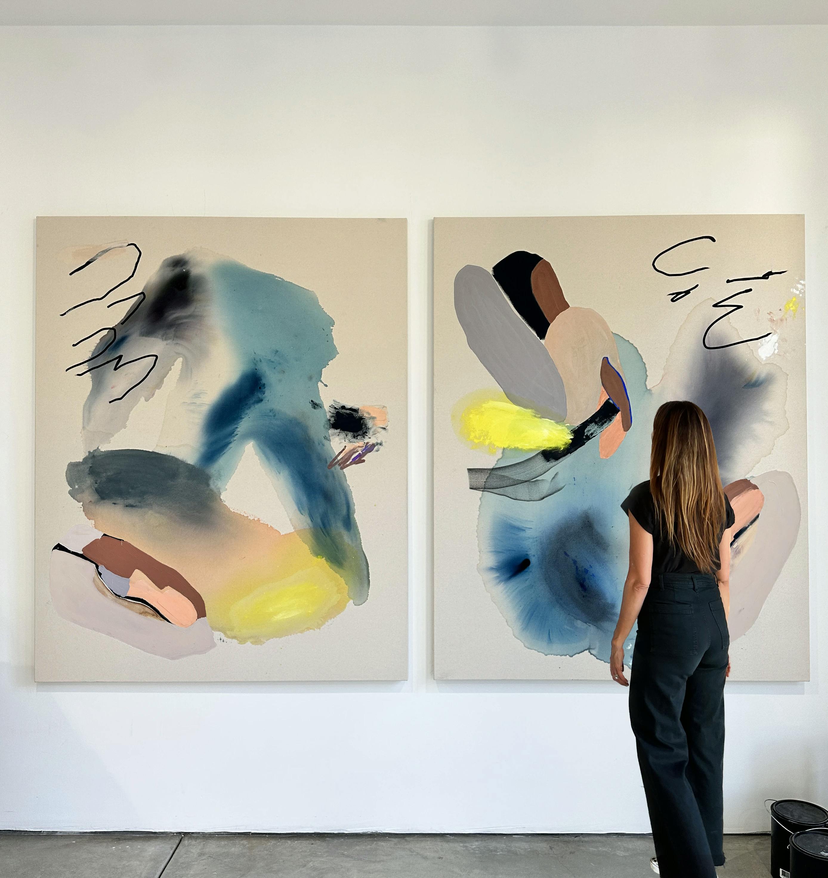 Artist Karina Bania standing in front of two abstract paintings in her studio. 