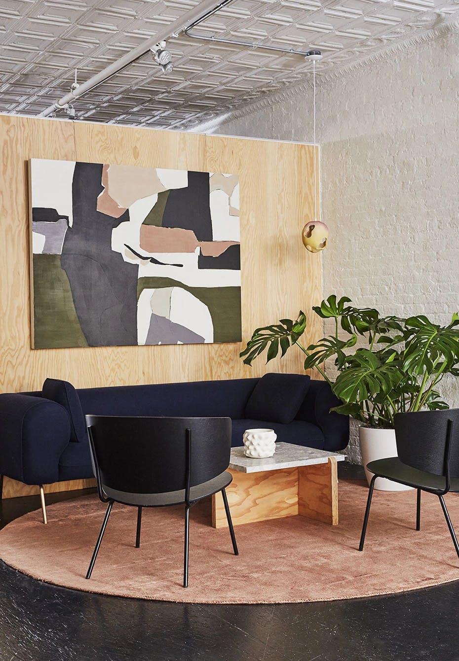 The lounge area at Uprise Art featuring a round, red rug, two black chairs, large monstera plant, and abstract painting by Holly Addi.
