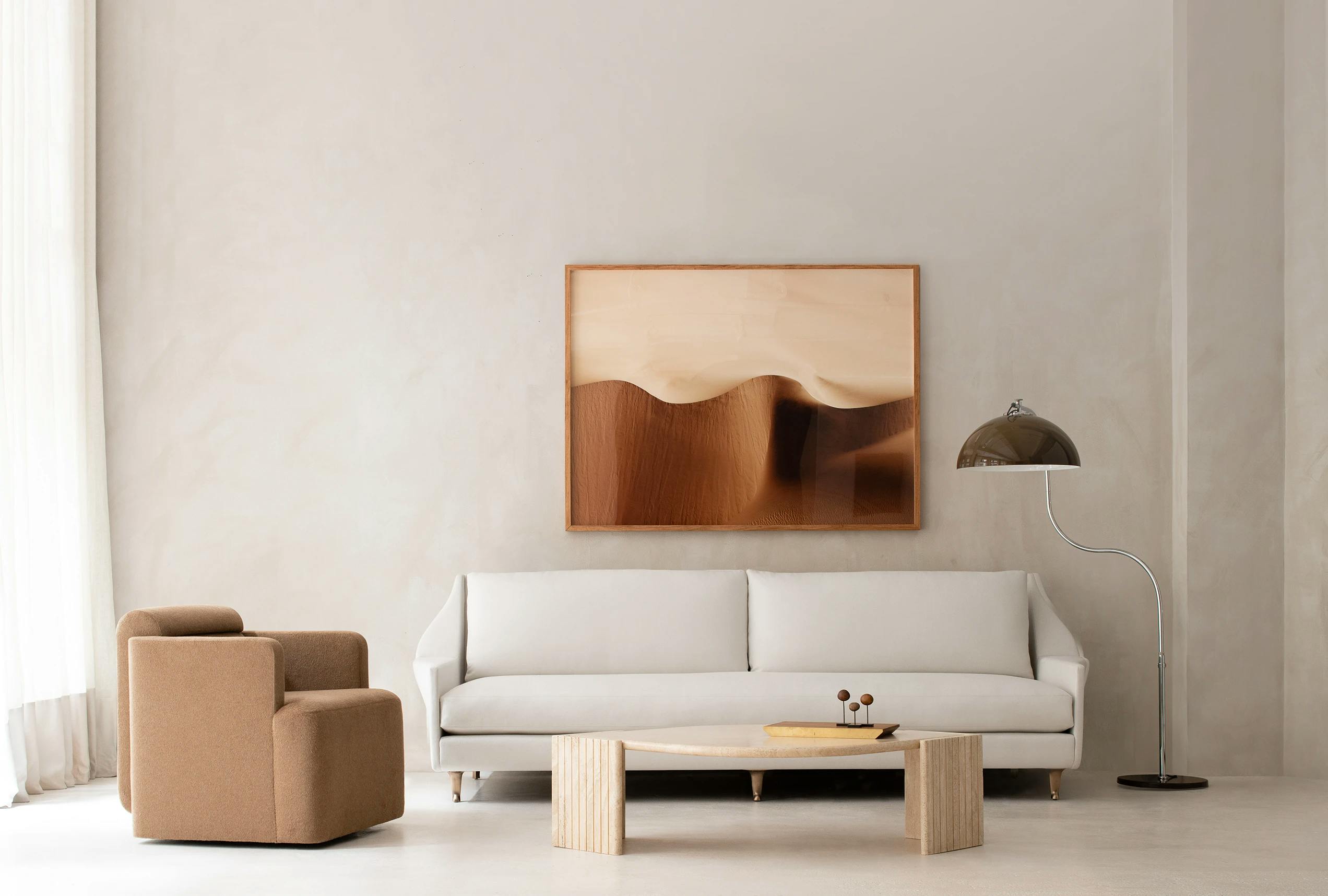 A neutral living room with brown armchair, white sofa, and a framed photograph of a desert by artist Brooke Holm.