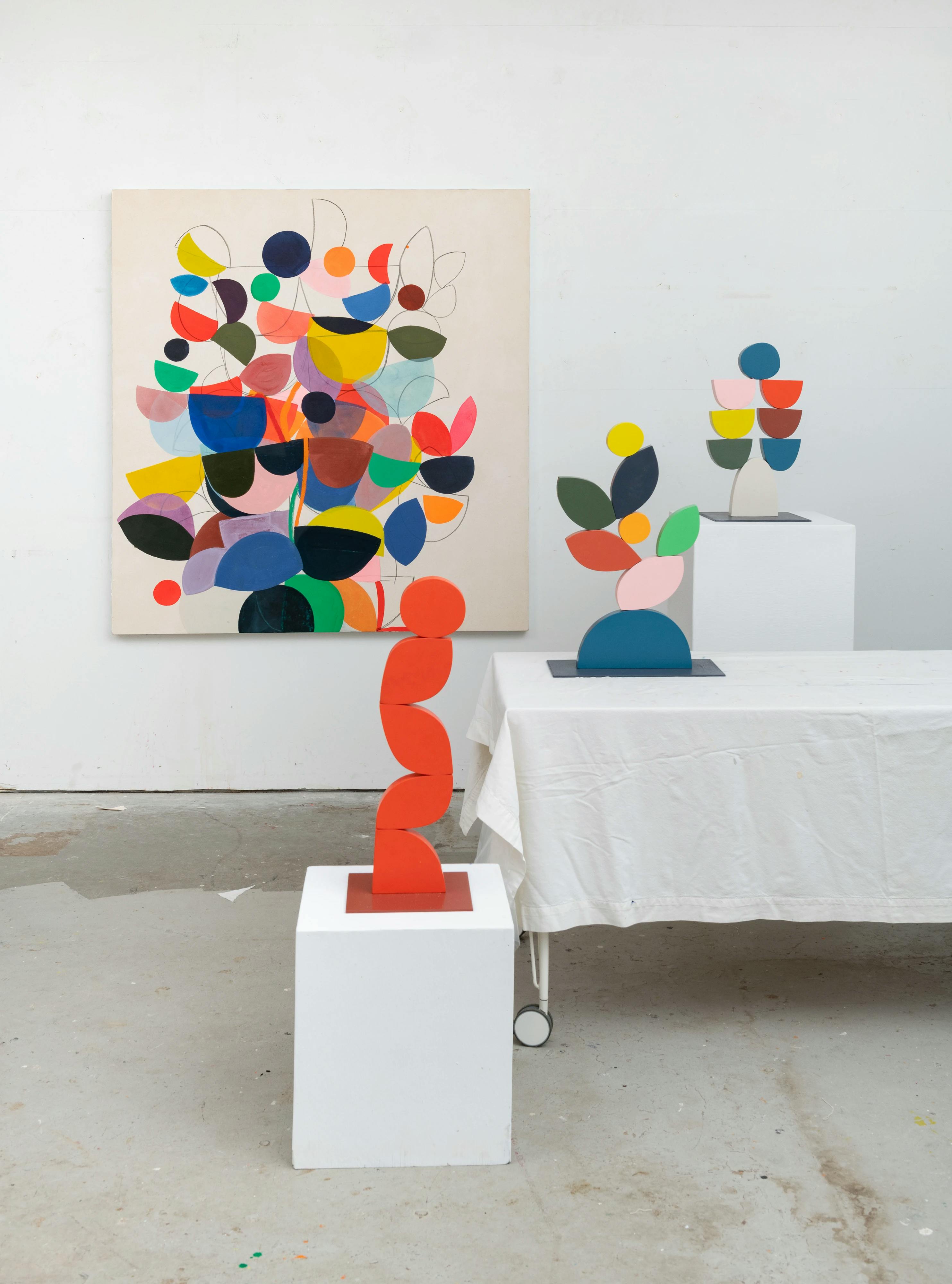 Three tabletop sculpture and one large colorful painting by artist Vicki Sher on display in her studio.