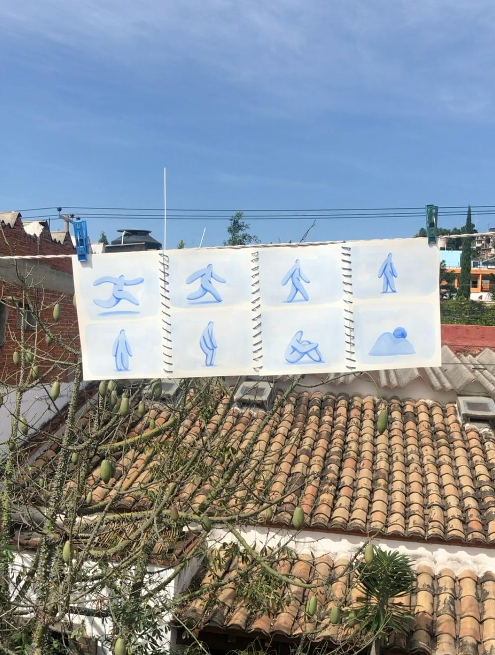Blue figurative drawings by artist Jocelyn Tsaih pinned on a clothesline suspended in the air above house roofs.