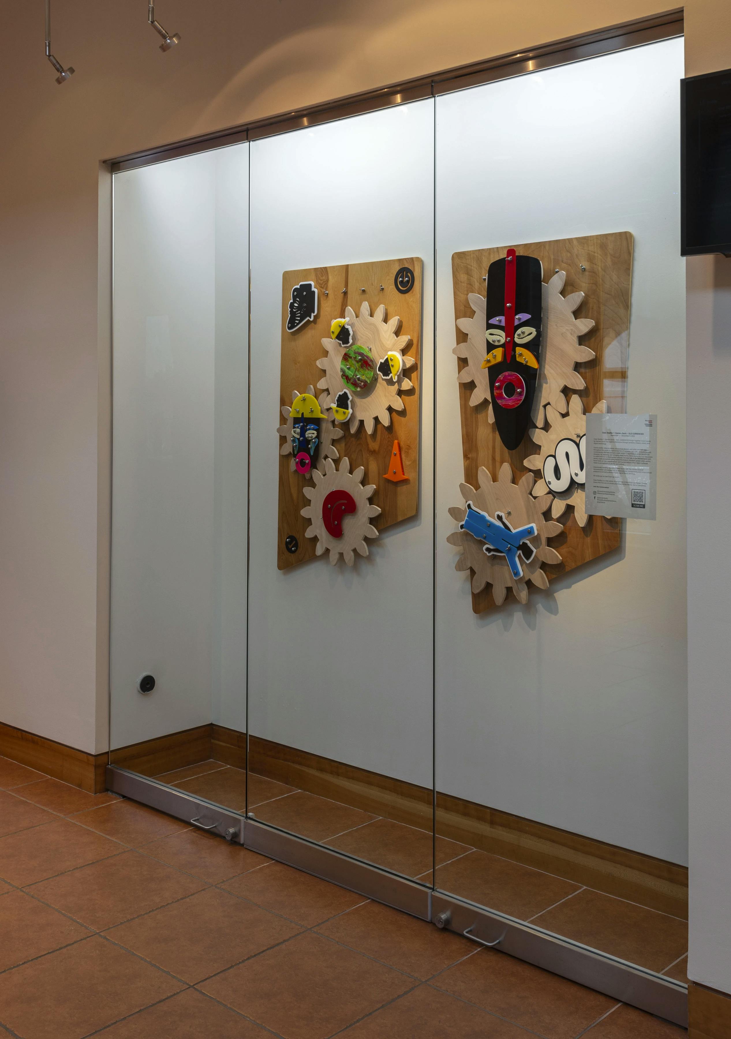 Two large, mixed-media wall sculptures by artist Damien Davis installed on a white wall behind a glass case at Montclair State University.