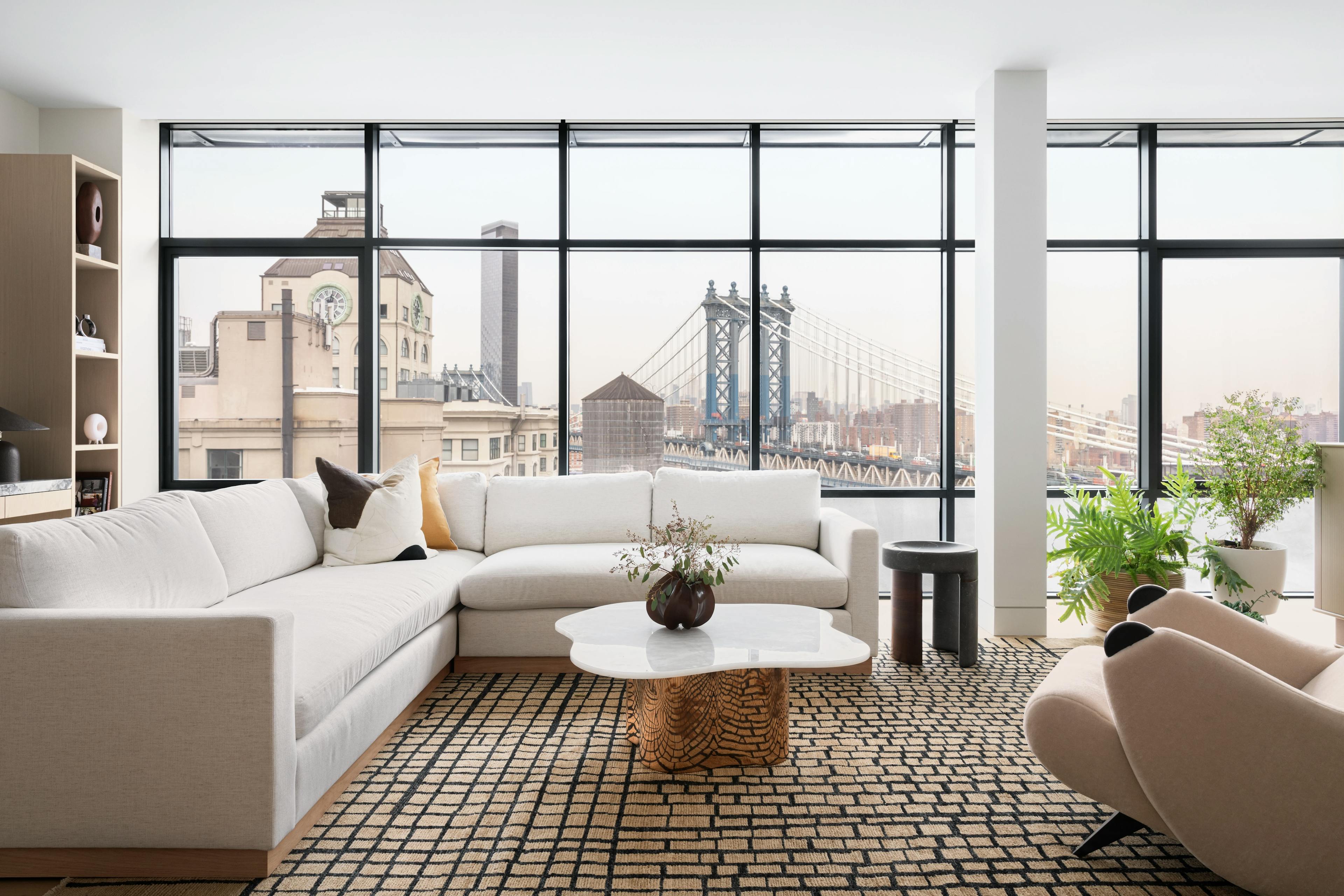 Modern living room with a white sectional sofa and floor-to-ceiling windows overlooking the Manhattan Bridge in the distance. 