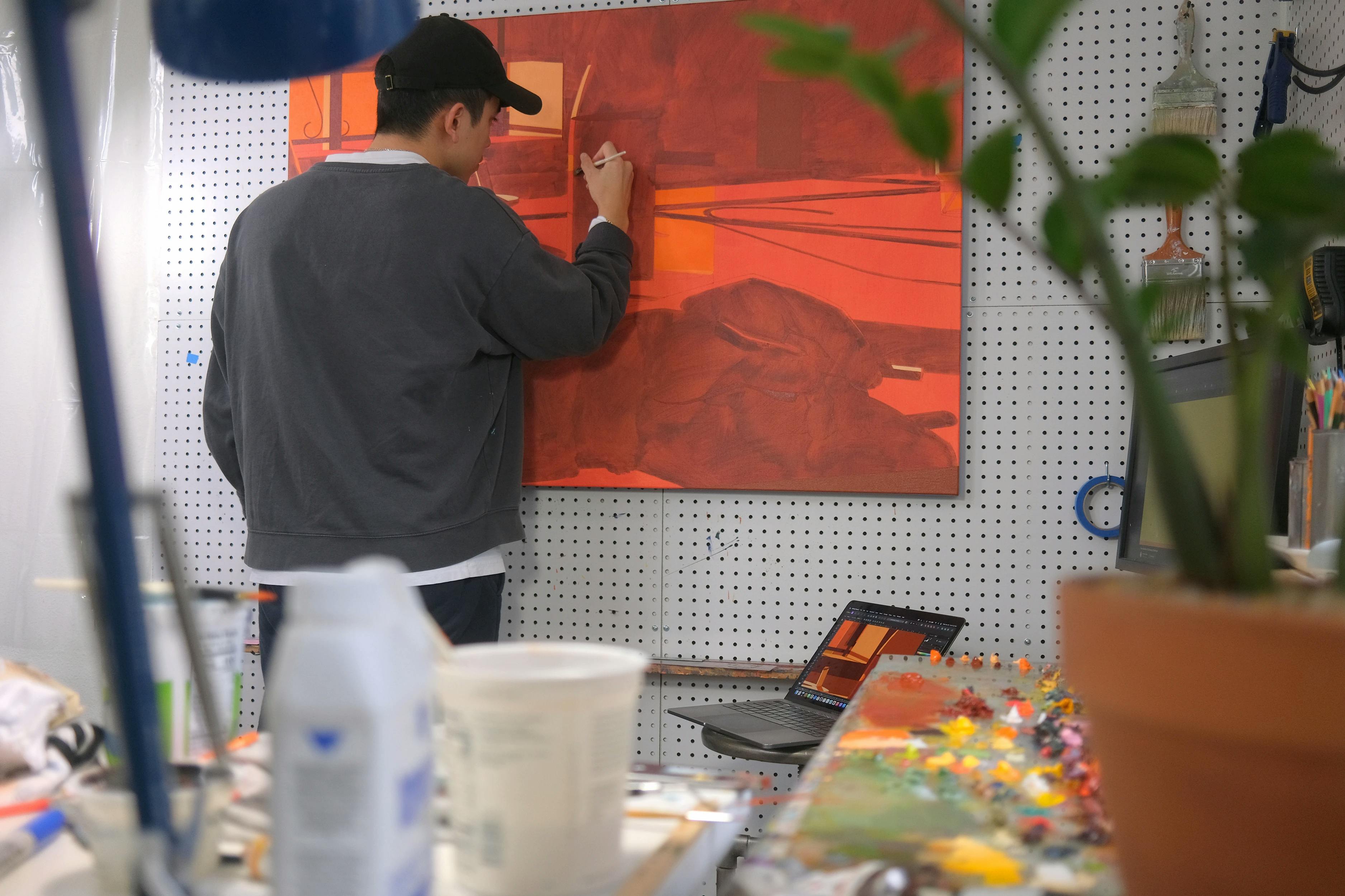 Artist Adrian Kay Wong working on an orange painting in his studio. 