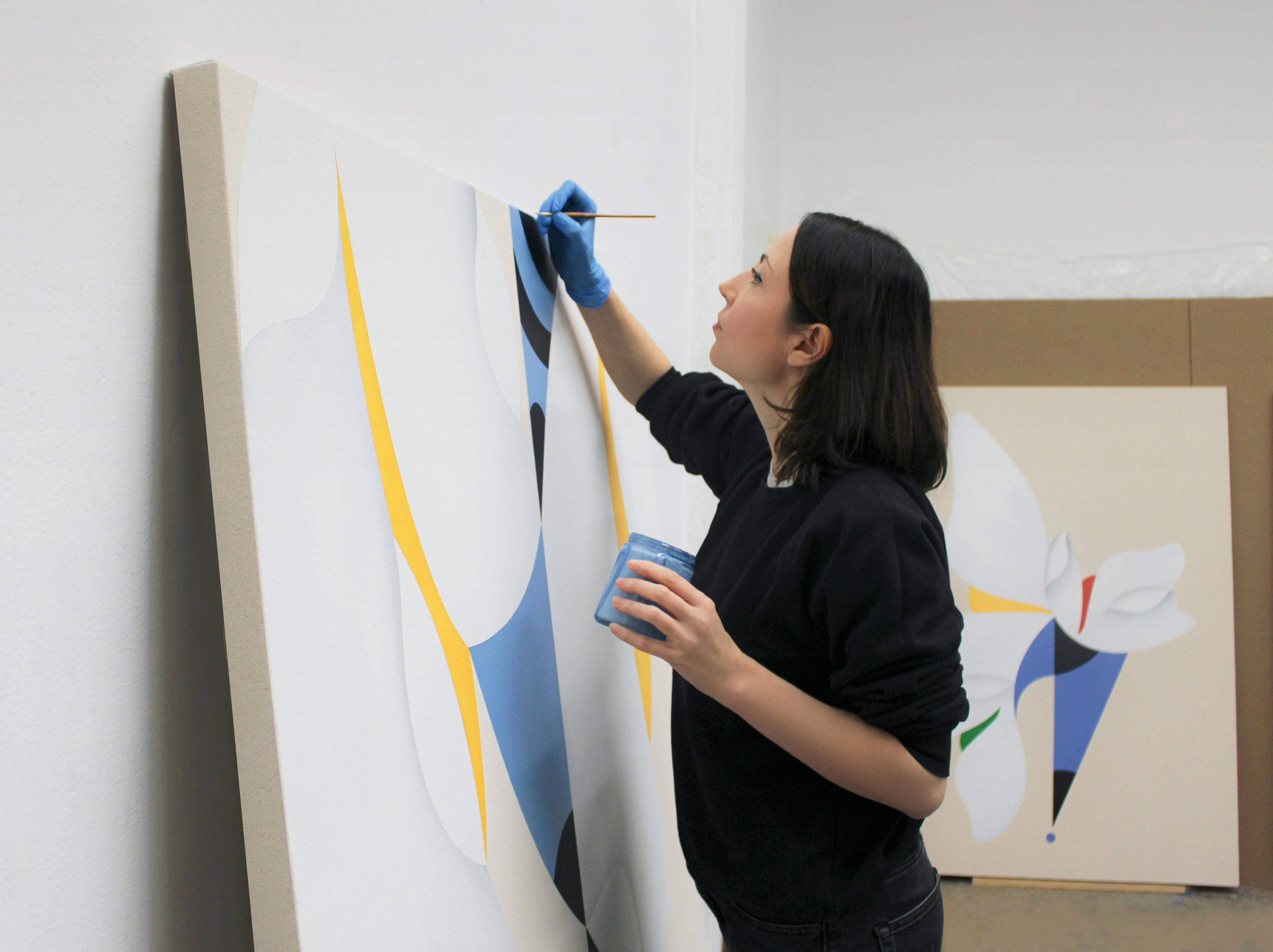 Artist Senem Oezdogan working on a large blue, yellow and white painting in her studio. 