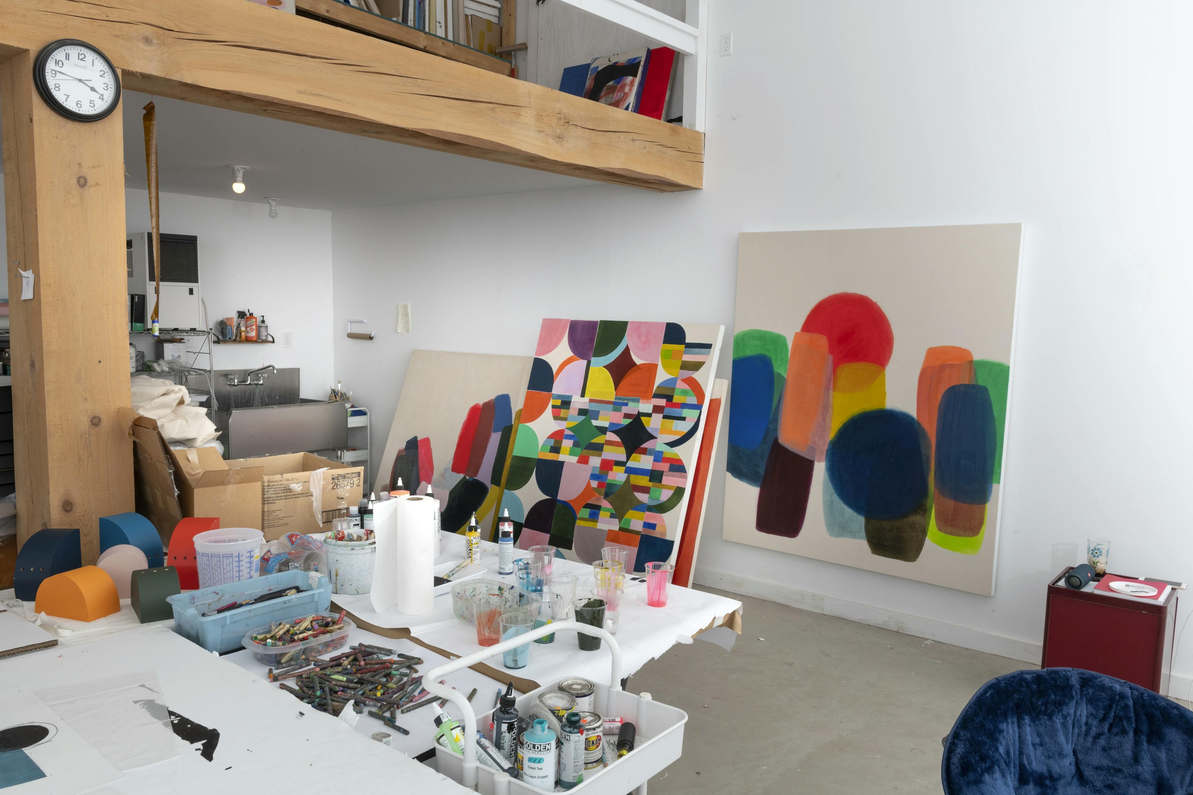 Large, abstract colorful paintings by artist Vicki Sher leaning against a white wall in her studio.