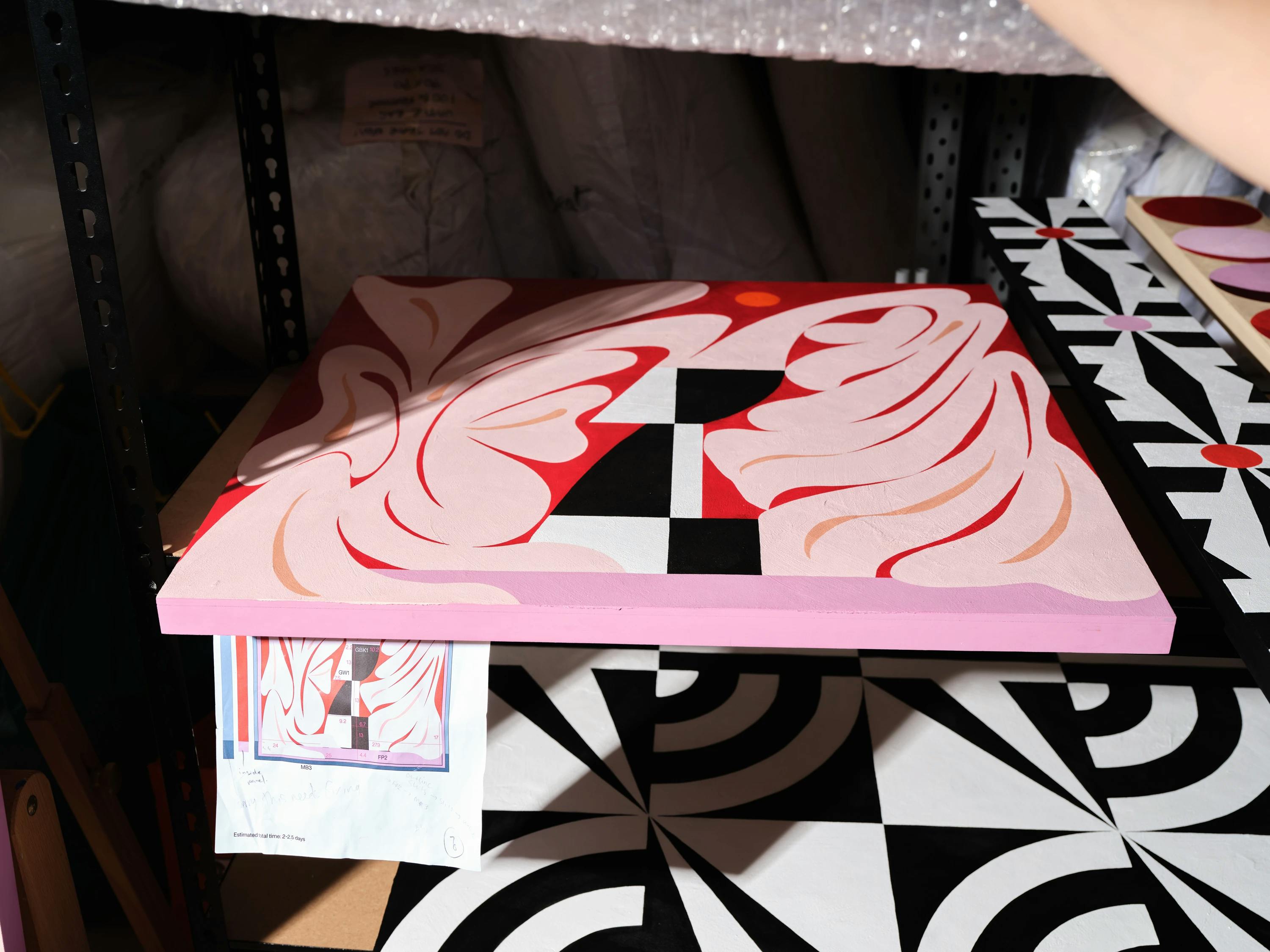 A pink, red, black and white painting on a shelf in Artist Evi O's studio.