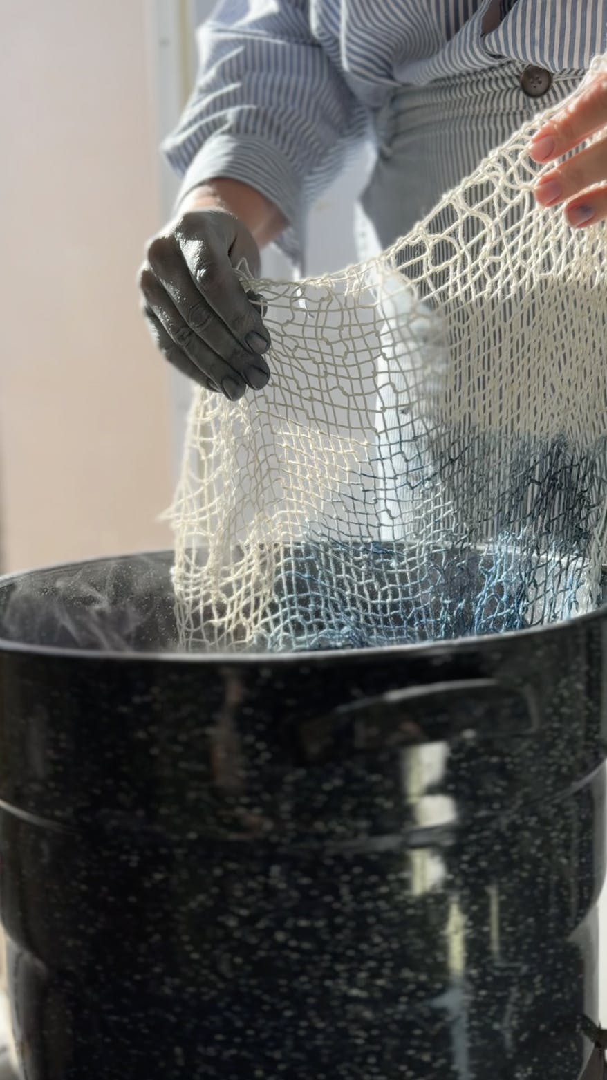 Artist Carrie Crawford naturally dyeing woven fabric in a large bucket.
