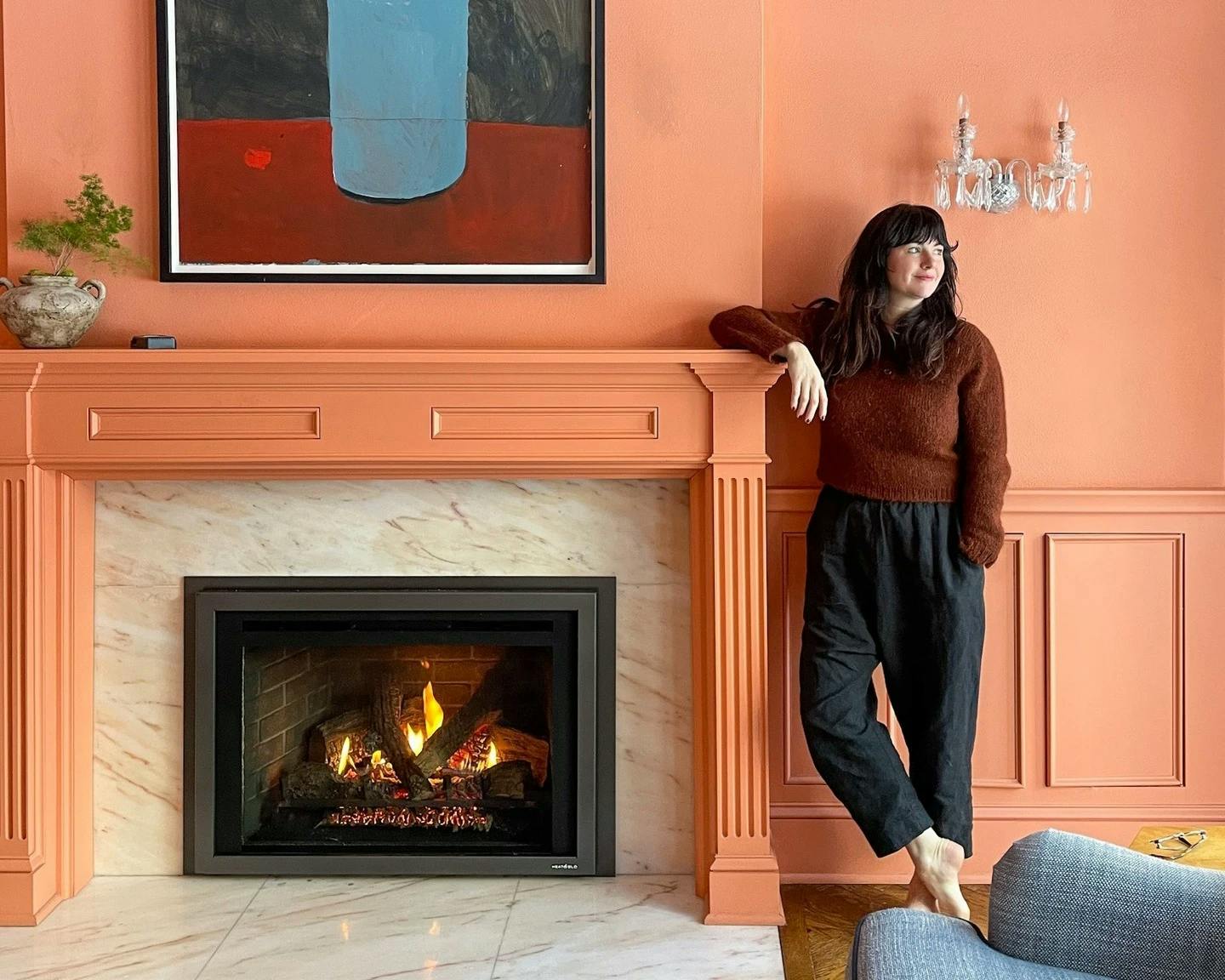 Kate Arends of Wit and Delight leaning against a fireplace mantle in a bright orange-colored living room.