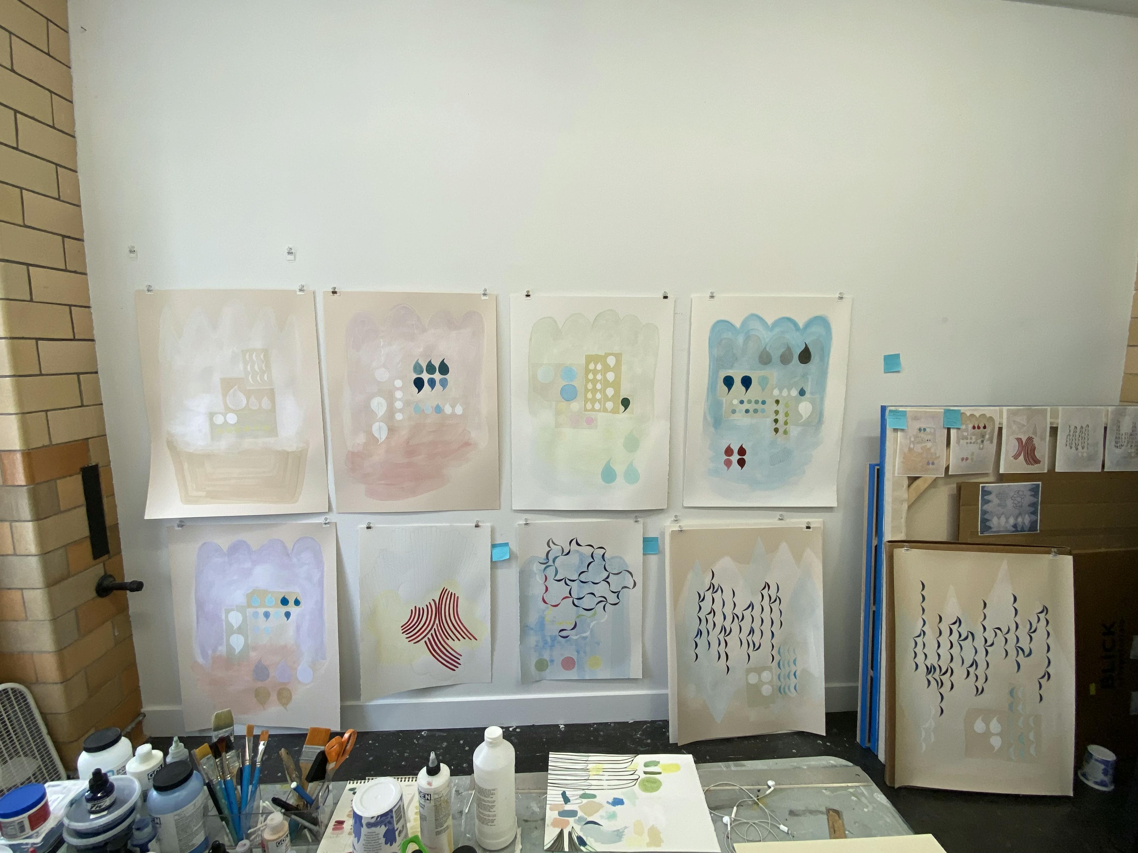 Abstract acrylic paintings by artist Lydia Bassis pinned to a white wall in her studio.