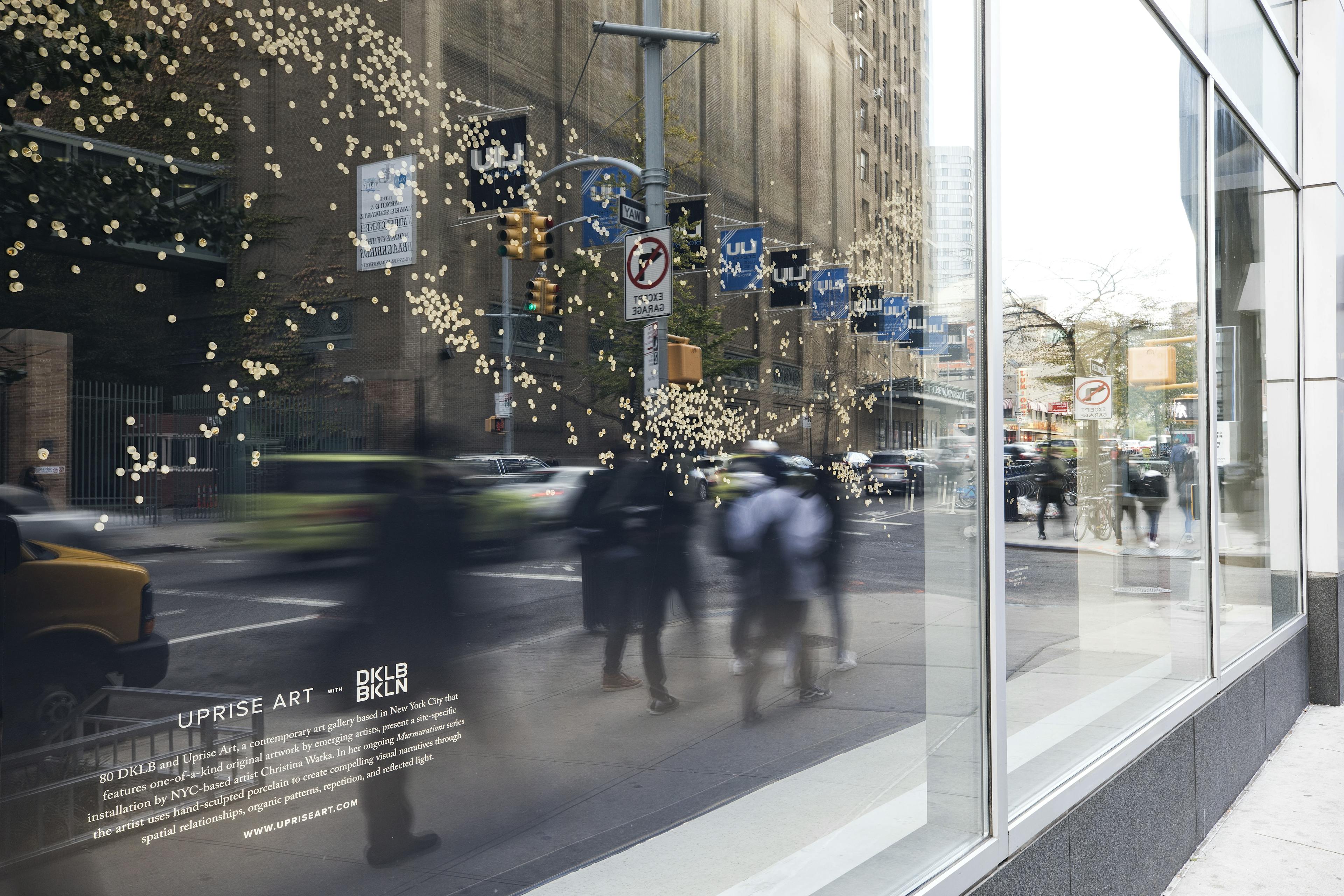 Floor-to-ceiling windows at DKLB BKLN reflecting a busy street with people walking and traffic lights.