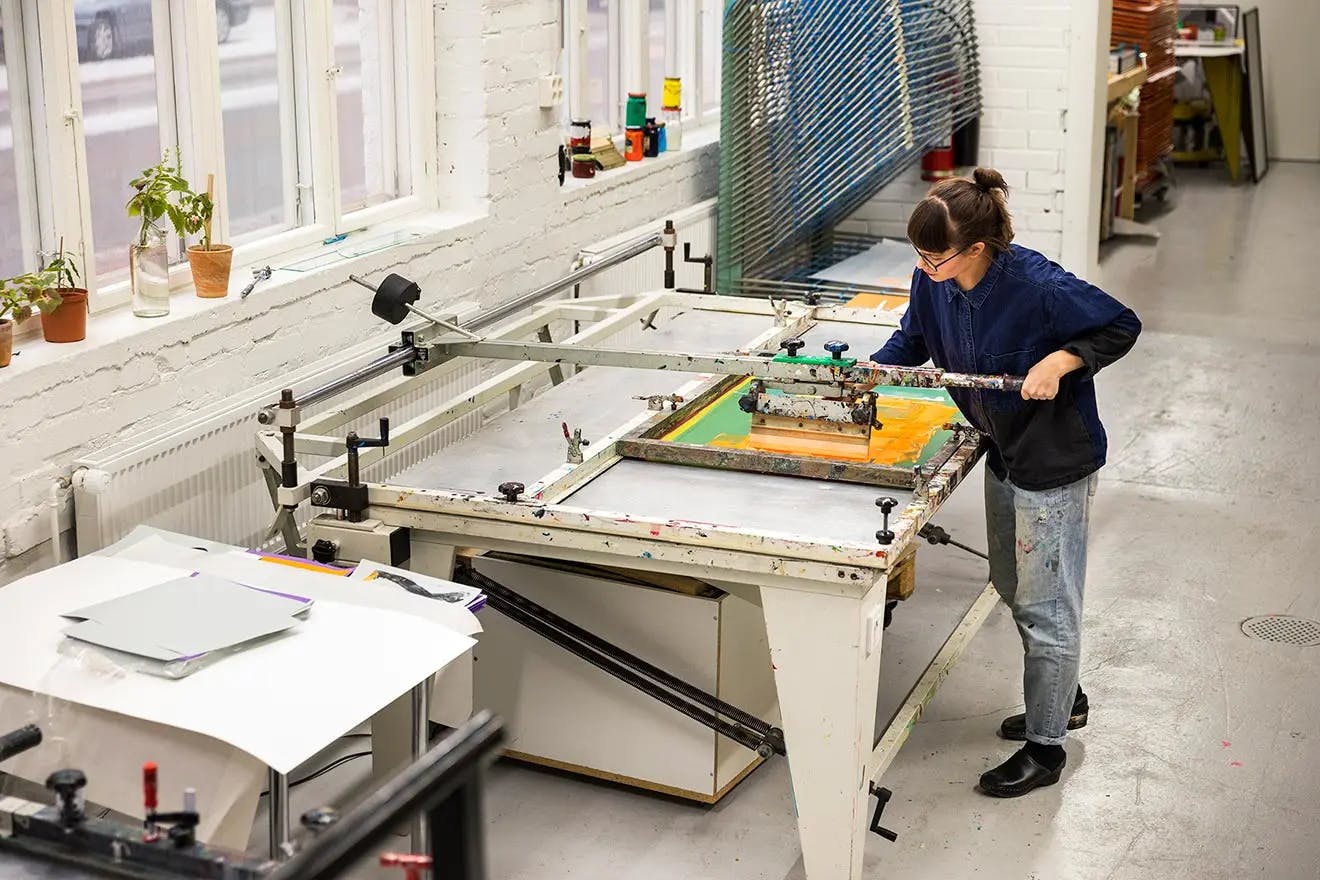 Artist Inka Bell using a printing press in a large studio.