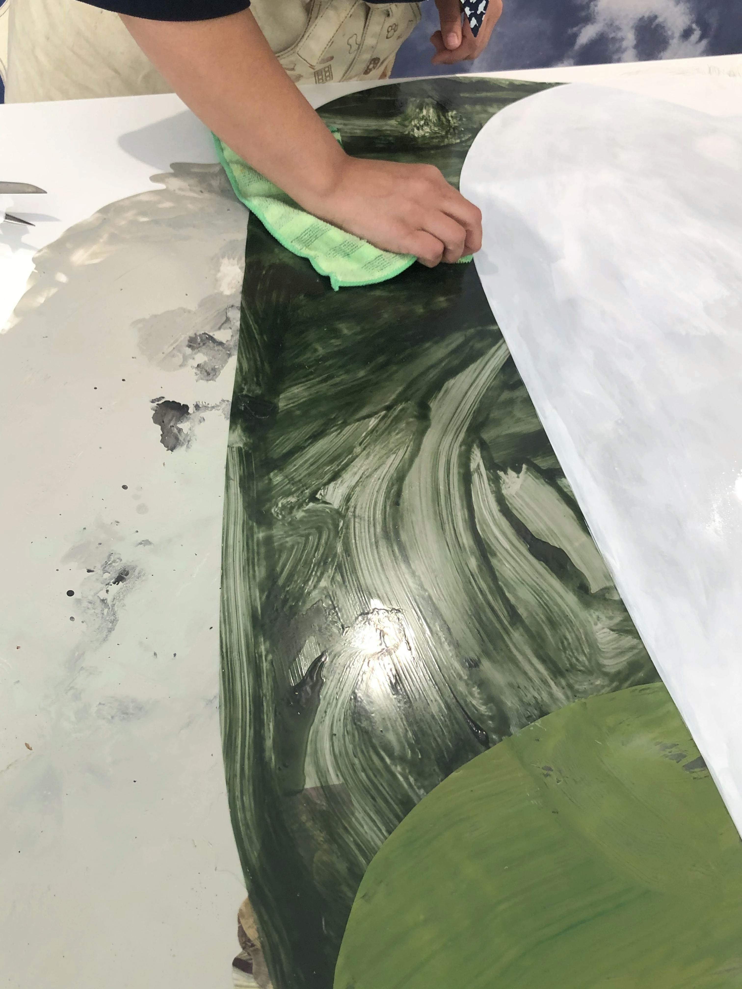 A close-up of artist Xochi Solis painting green ink on a piece of paper in her studio.