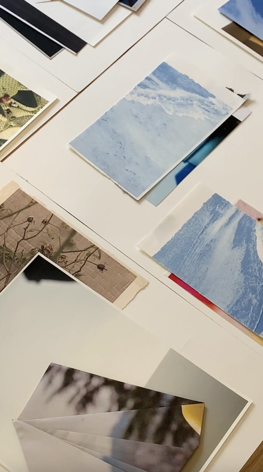 Layered groupings of prints and photographs by artist Carmen Vela on a white table in her studio.