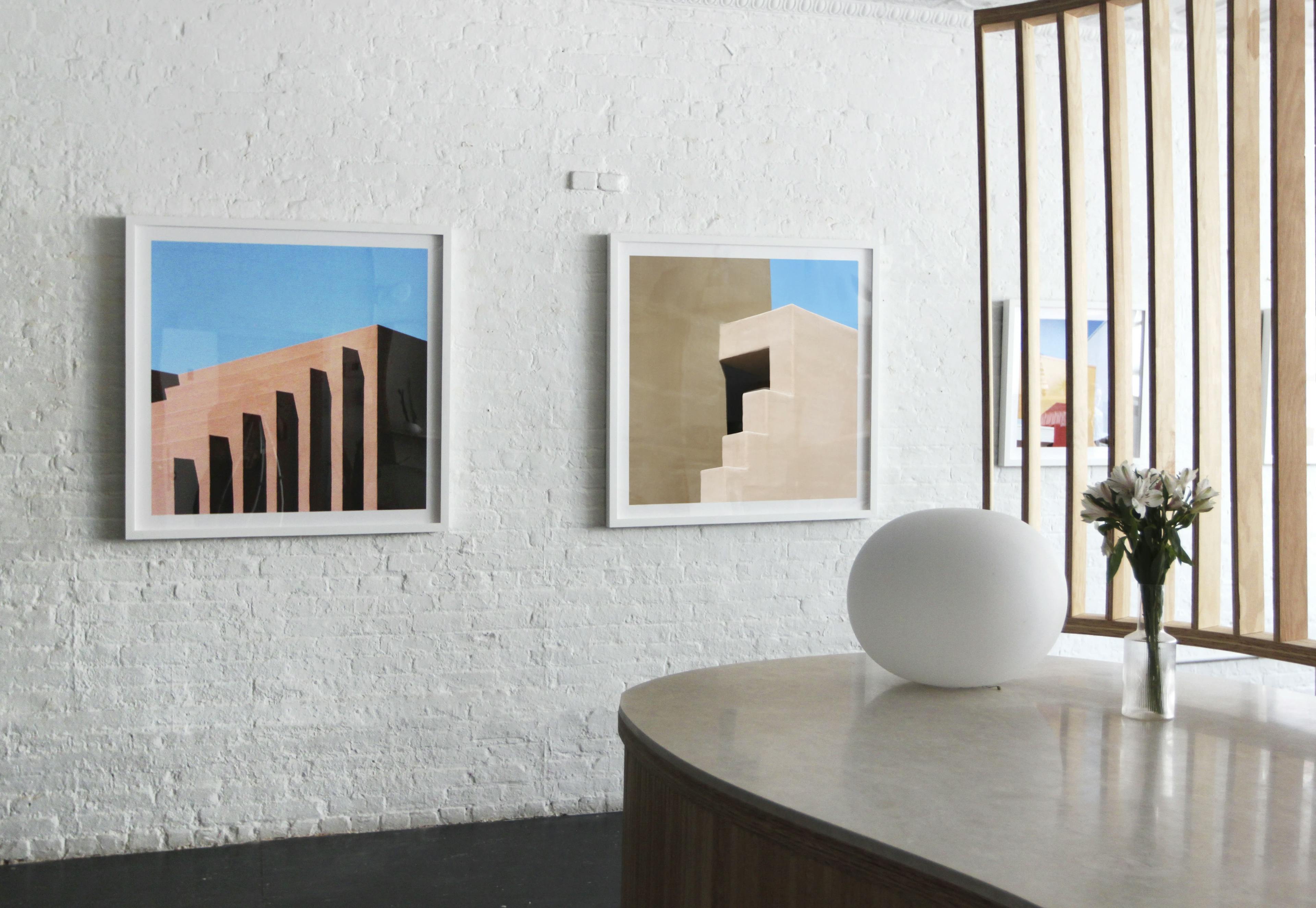 Three framed photographs of exterior architecture by artist Sinziana Velicescu installed on a white brick wall at the Uprise Art showroom.