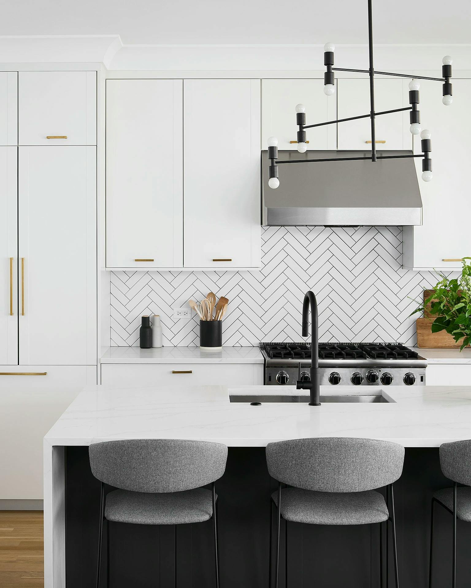 A modern kitchen with white cabinets, a white herringbone backsplash and black finishings in a Chicago apartment.