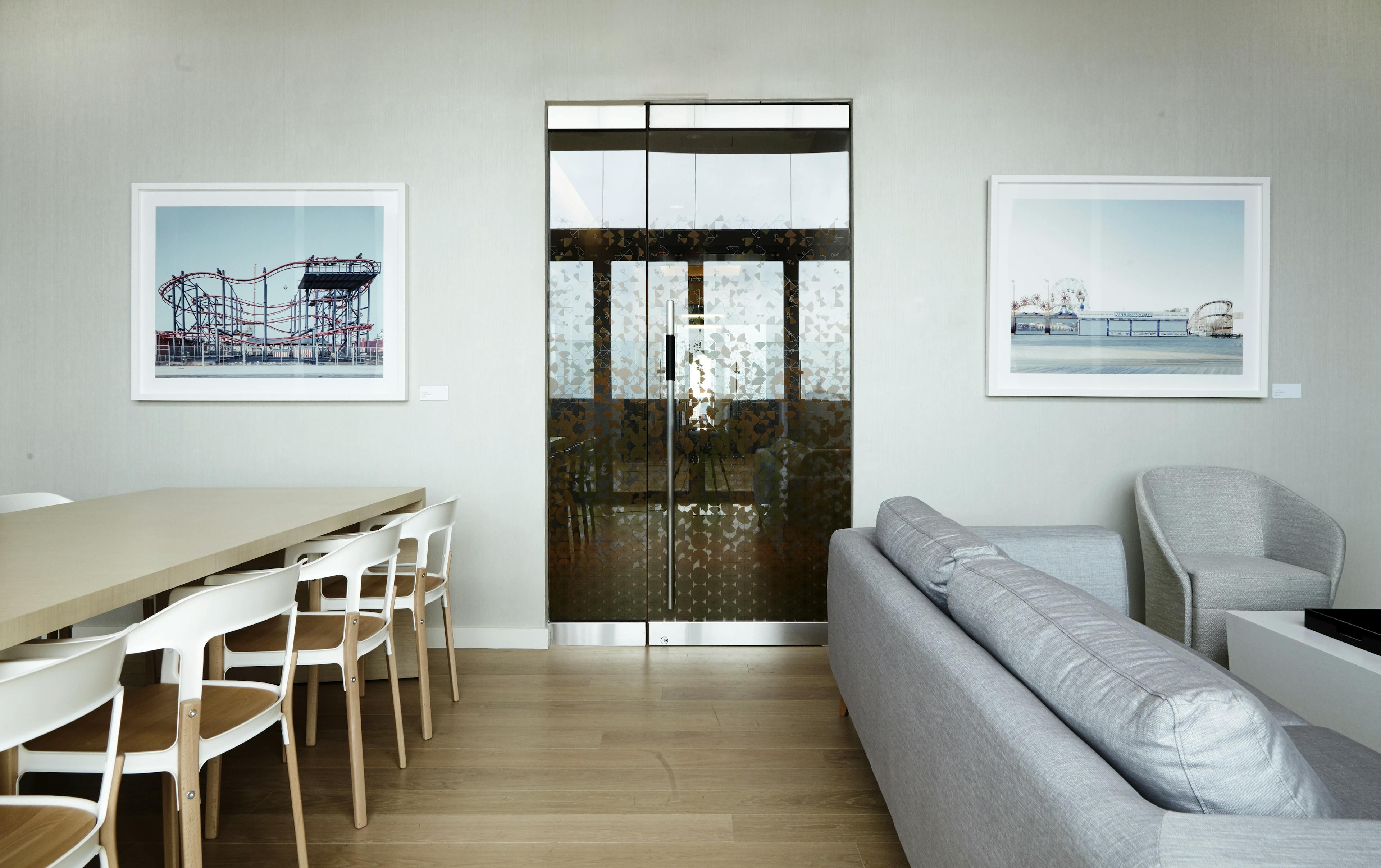 Two framed photographs of amusement parks installed on either side of a glass door in the lounge area of a residential building.