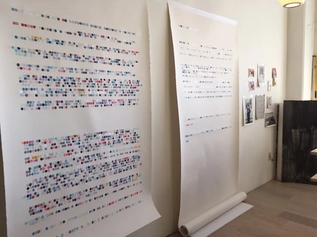 Large scrolls of paper with color-coded dots installed on a white wall in artist Gail Tarantino's studio.