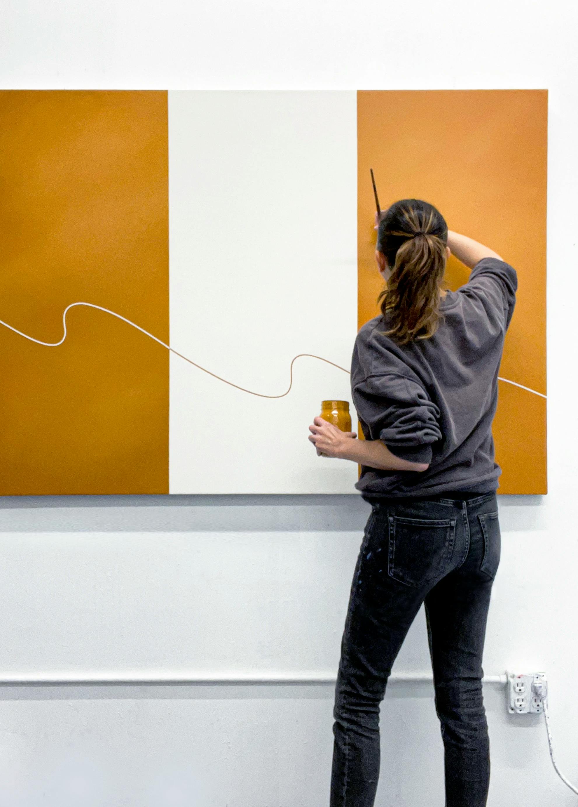 Artist Senem Oezdogan painting on a large, striped orange and white canvas in her studio.