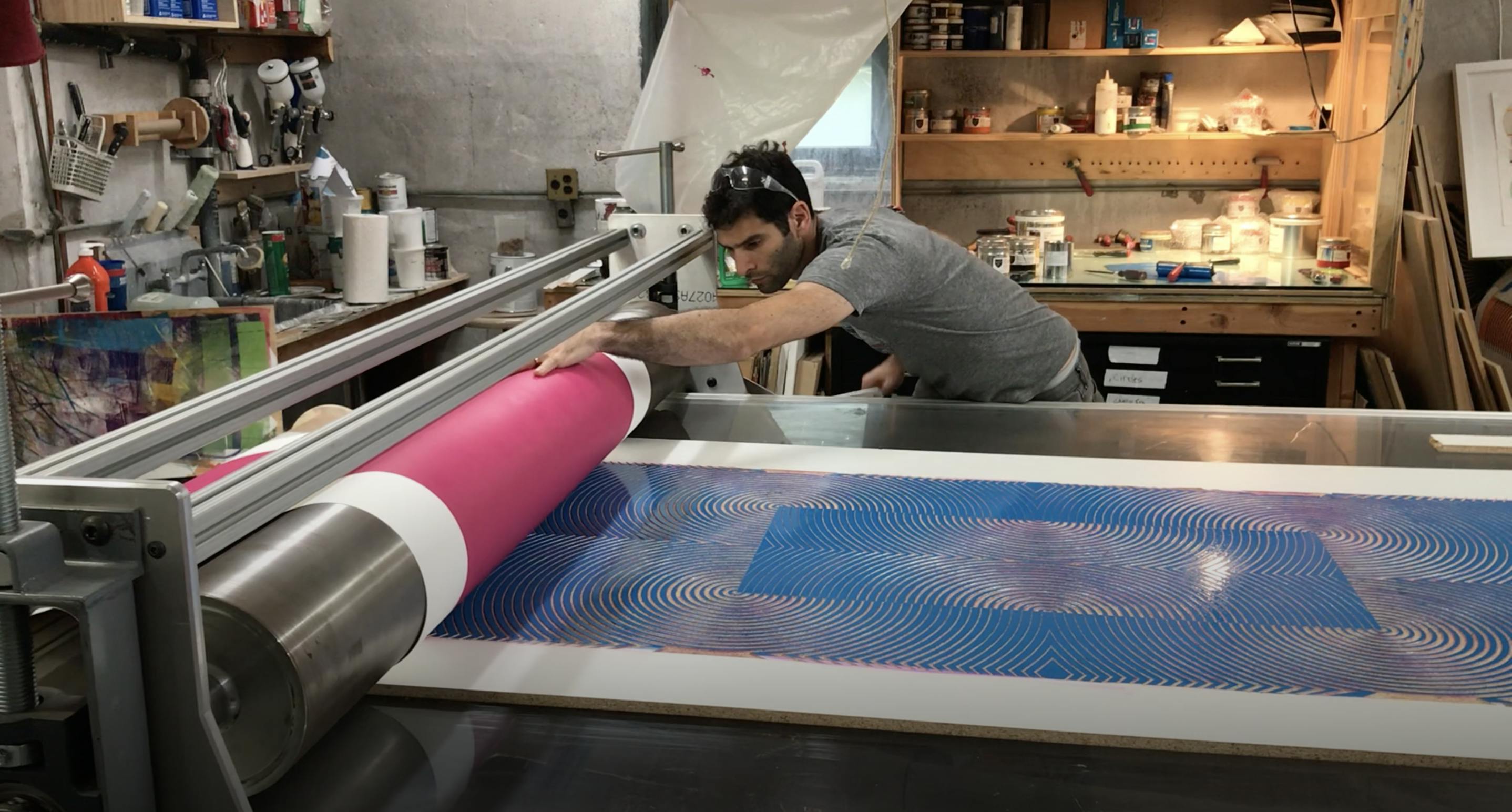 Artist Matt Neuman working on a large printing press in his studio.