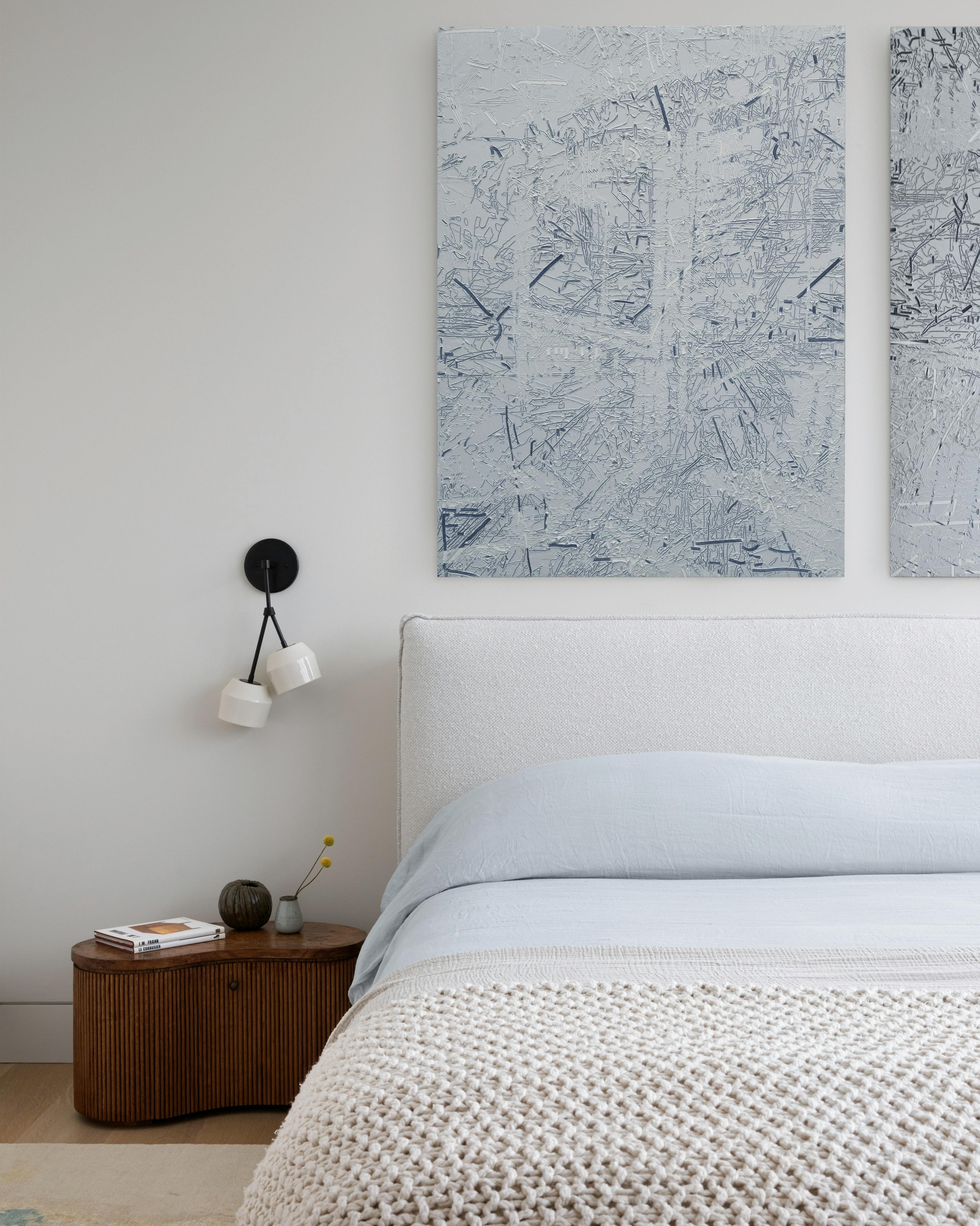Textured gray, heavy impasto diptych by artist Blake Aaseby installed above a bed with a knitted beige blanket.