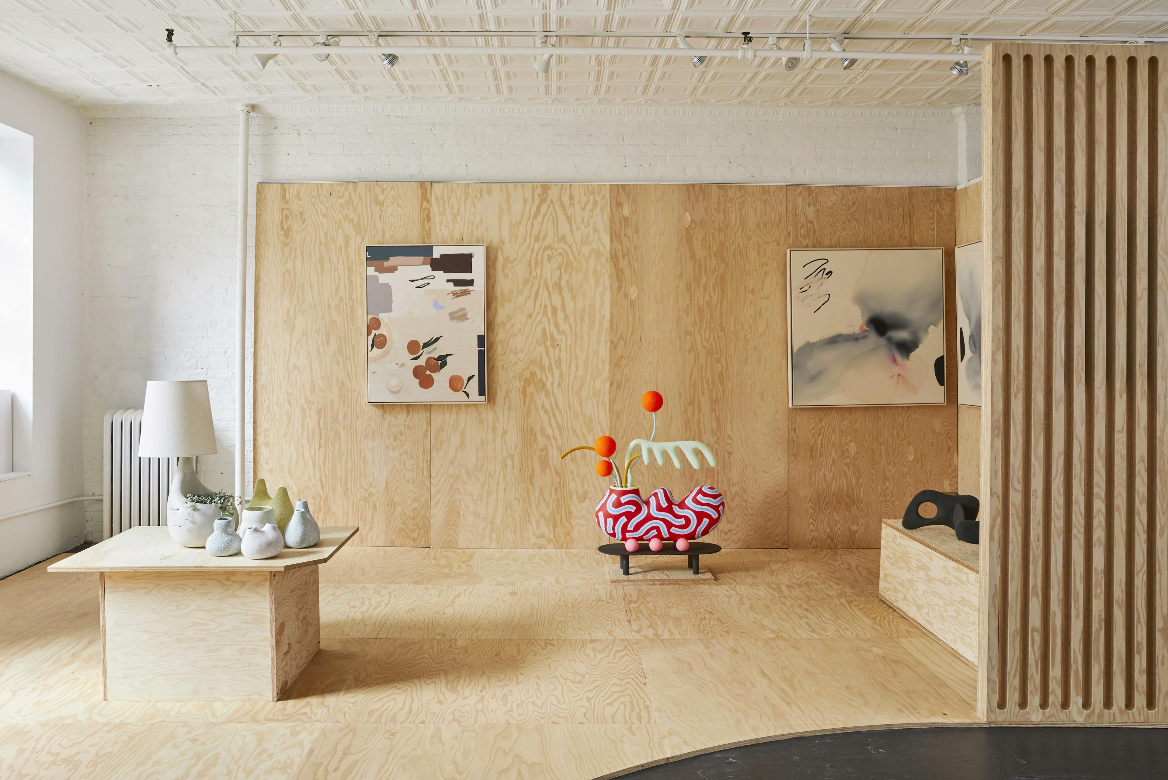 Raw plywood covers the walls and floors to create an exhibition space at Uprise Art, filled with abstract paintings and sculptures.