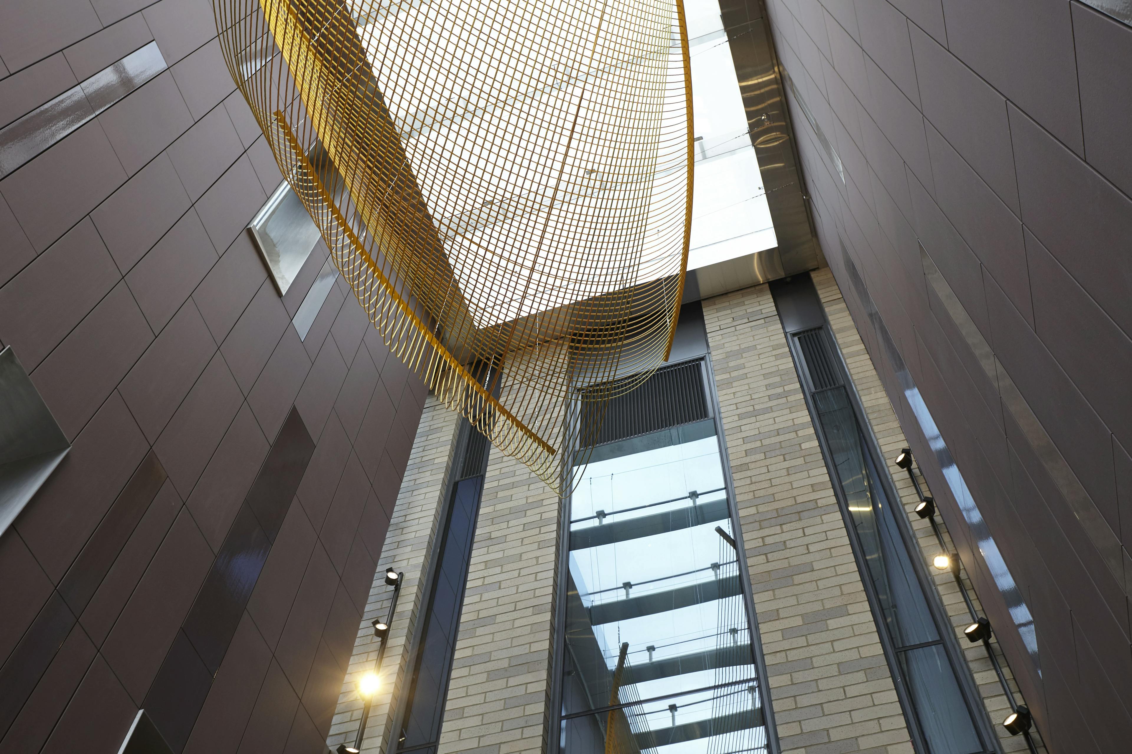 Site-specific installation of golden rope and steel by artist Rachel Mica Weiss suspended in the lobby of a modern building.