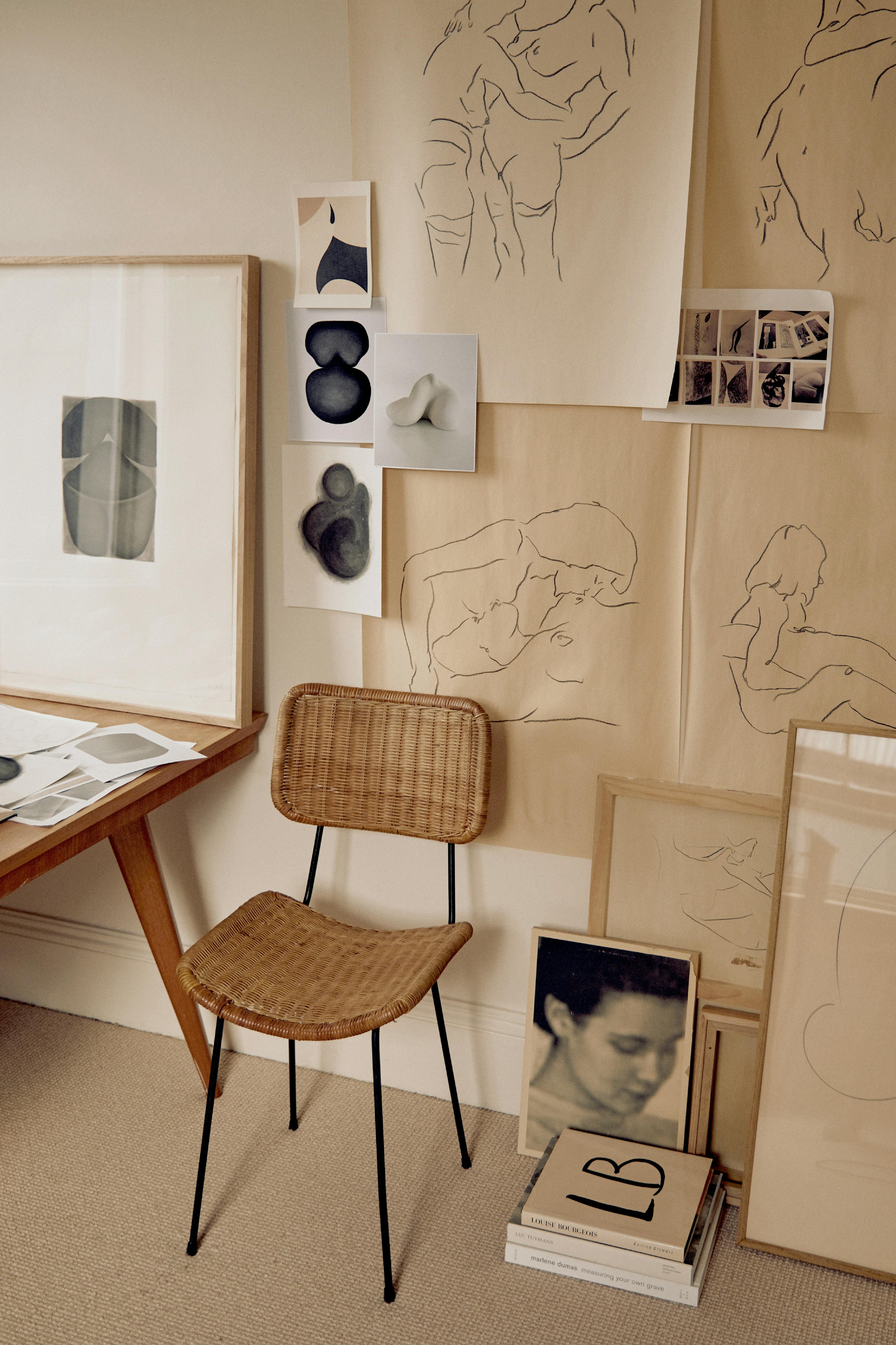 Caroline Walls' studio, with various drawings pinned to the wall and a rattan chair next to a wood table.