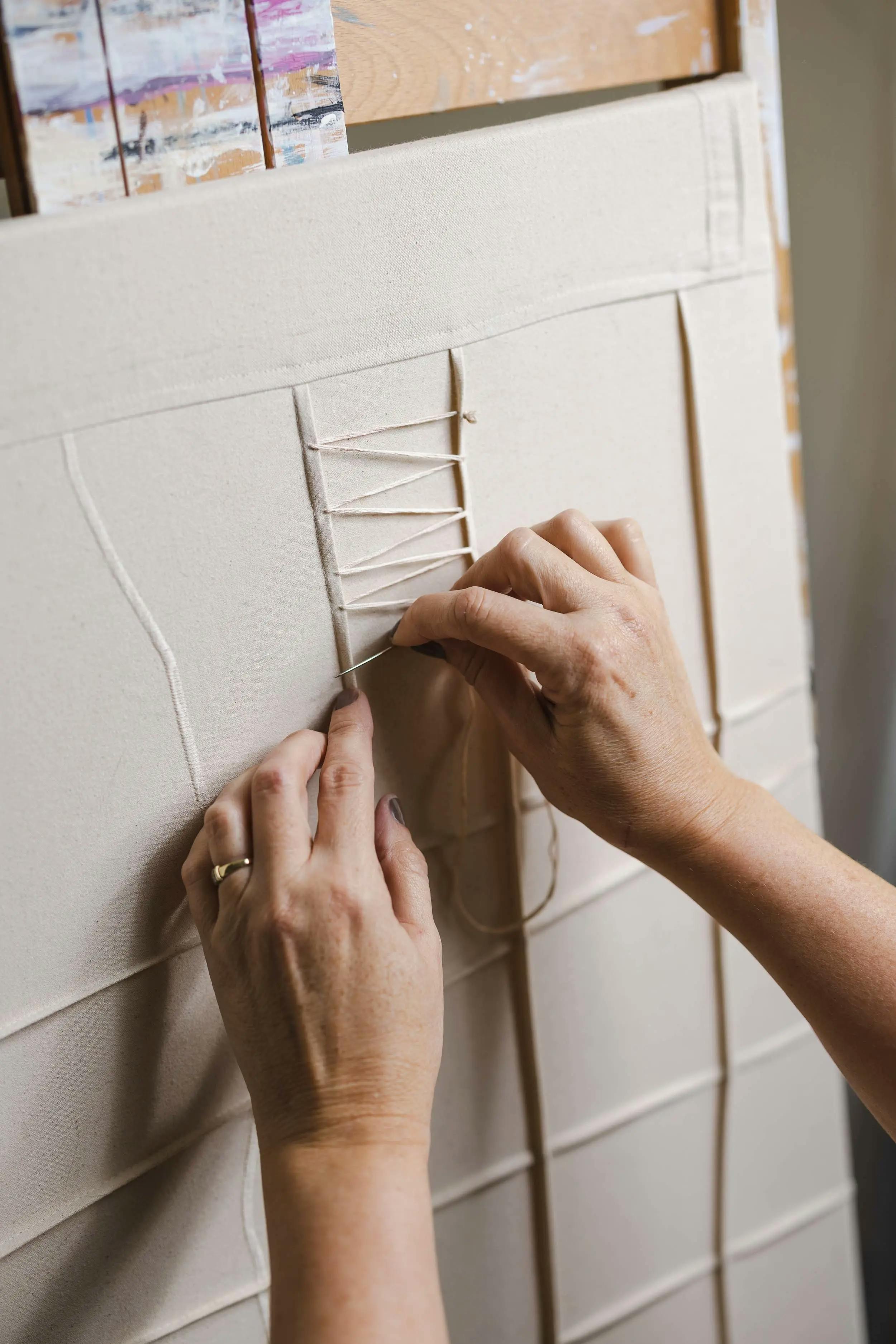A close up of artist Nicole Anastas threading white embroidery floss through a textured, neutral canvas.