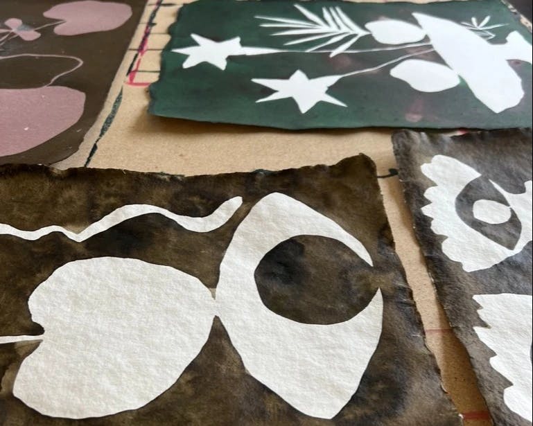 Multiple paintings by artist Kate Roebuck, some with eye motifs and some with stars, laid out on a table in her studio.